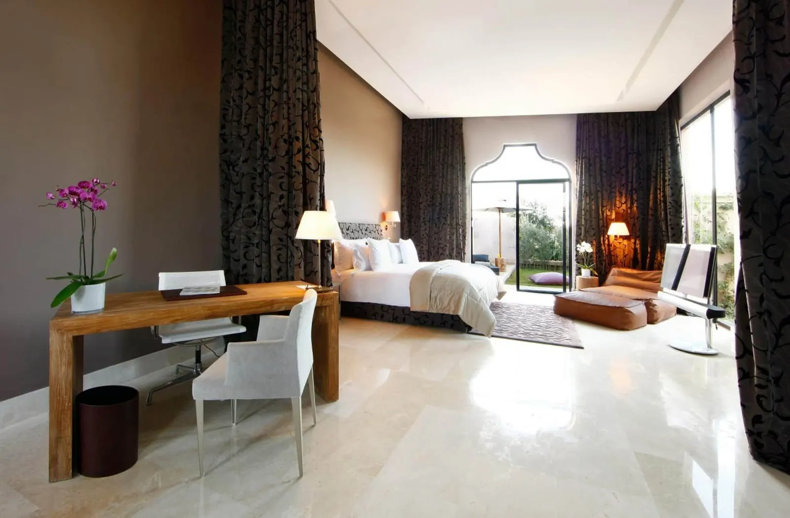 Junior Suite at Palais Namaskar: a large marble-floored room with a desk in front and a king bed by tall glass doors