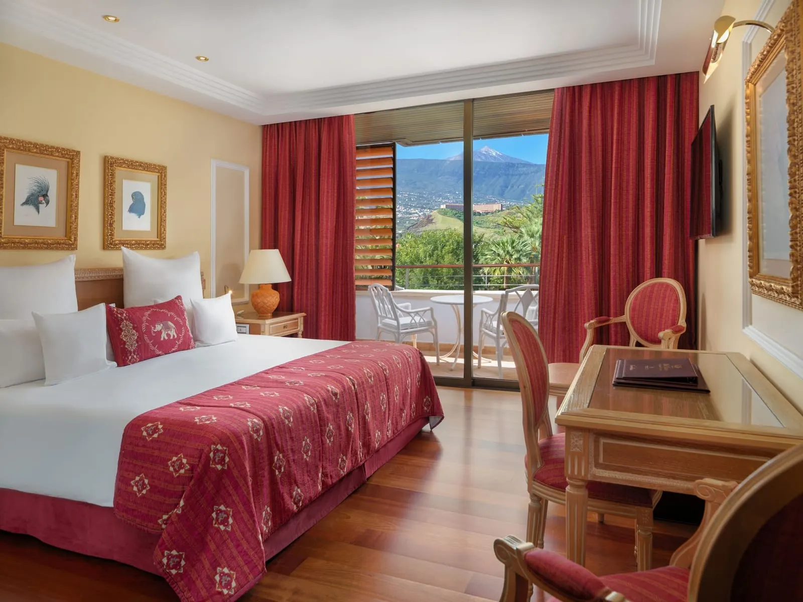 Deluxe Teide View at Hotel Botánico: a king bed with a red bedspread and a balcony door framing Mount Teide
