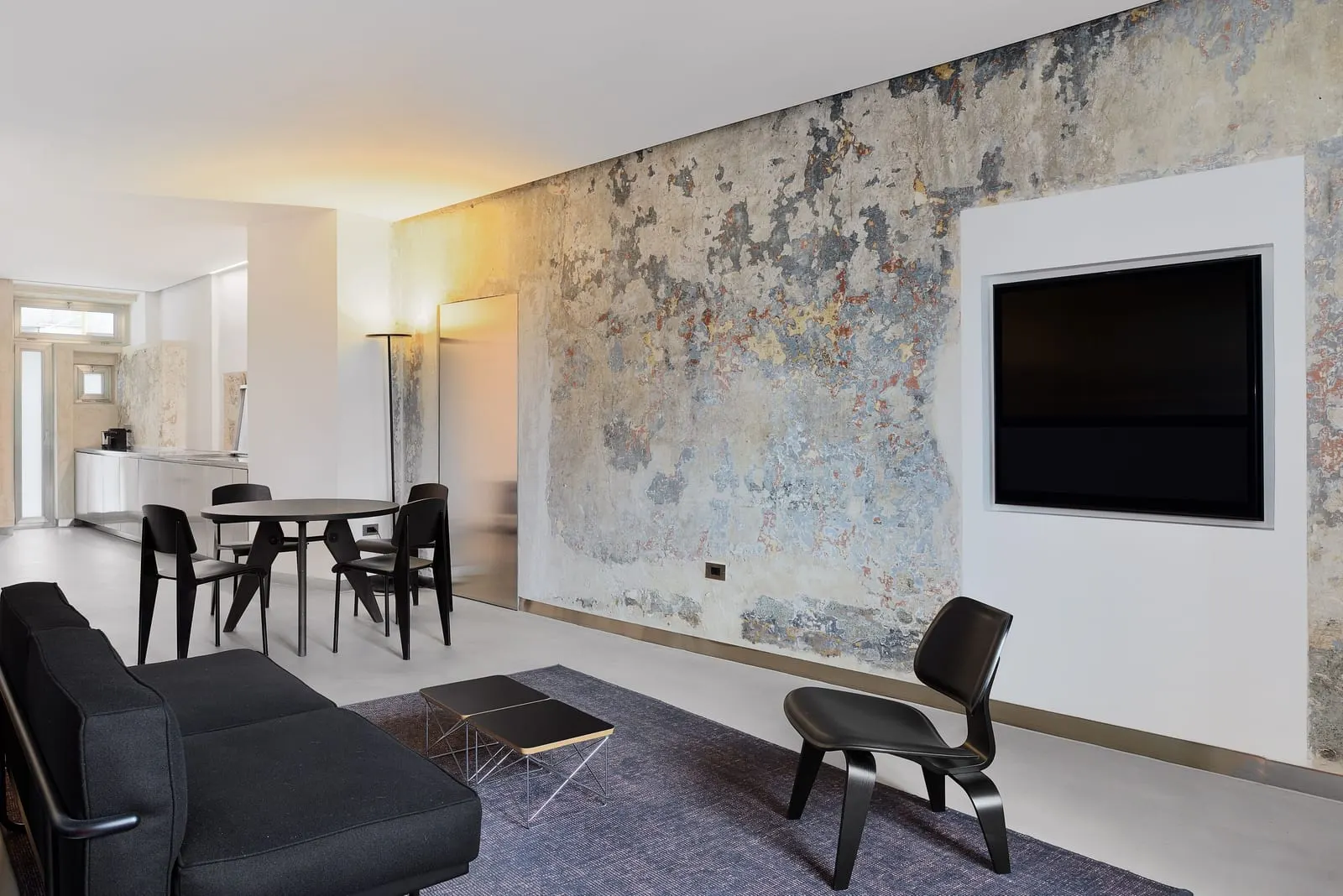 Master Suite Apartment at Rhinoceros Roma: a black sofa, a dining table and a weathered painted wall with a TV