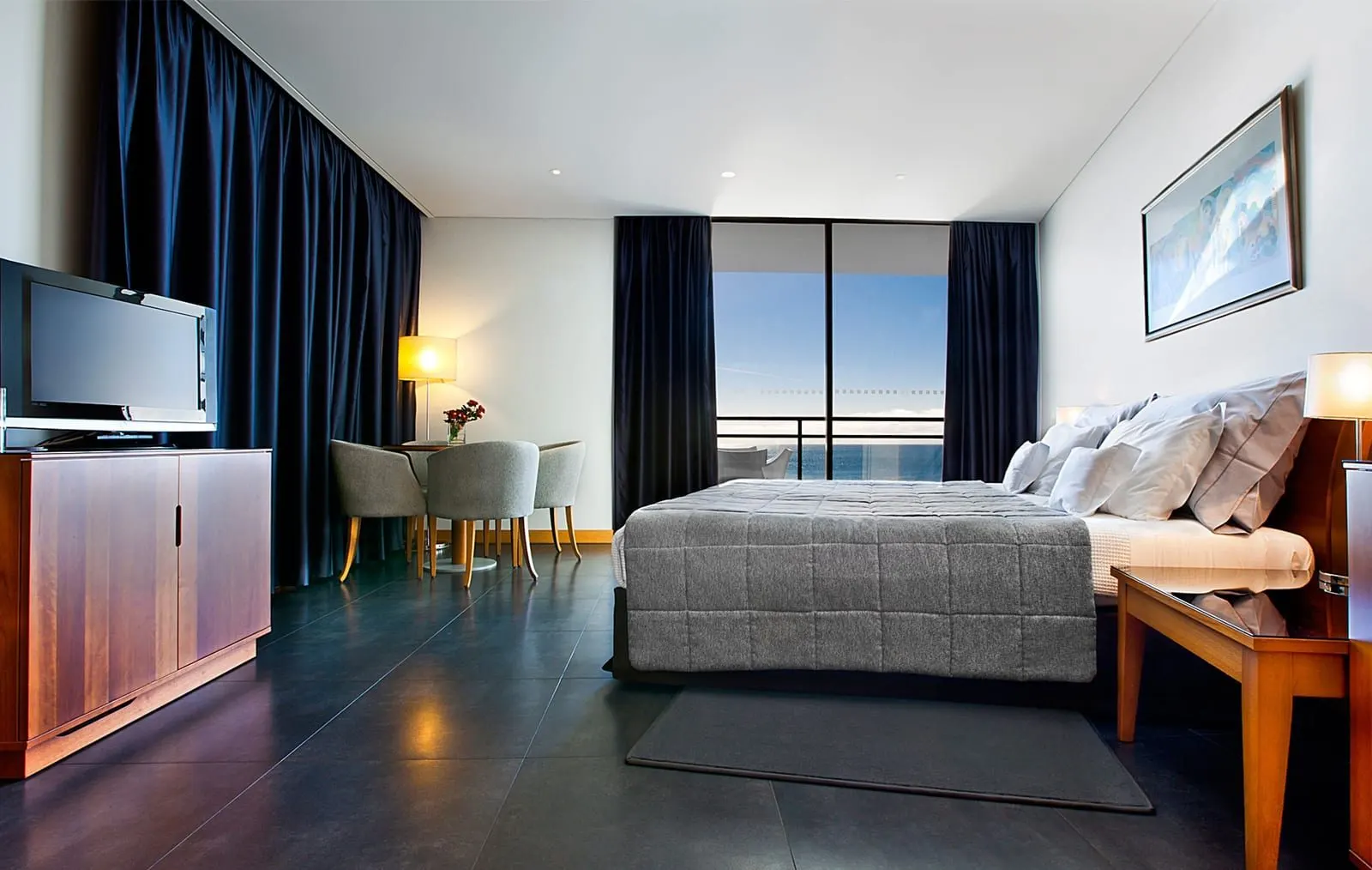 Premium Family Sea View Room at VidaMar Resort Hotel Madeira: a king-size bed, a round dining table with four chairs and a glass door to a balcony over the sea