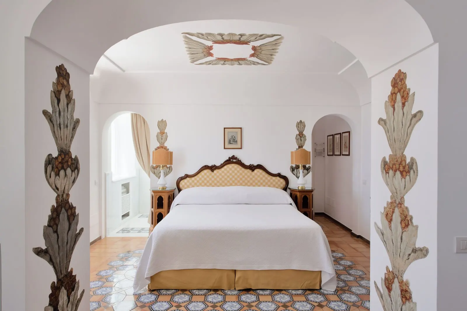 Junior Suite Superior Sea View at Le Sirenuse: a double bed with a carved headboard in an alcove framed by painted floral columns