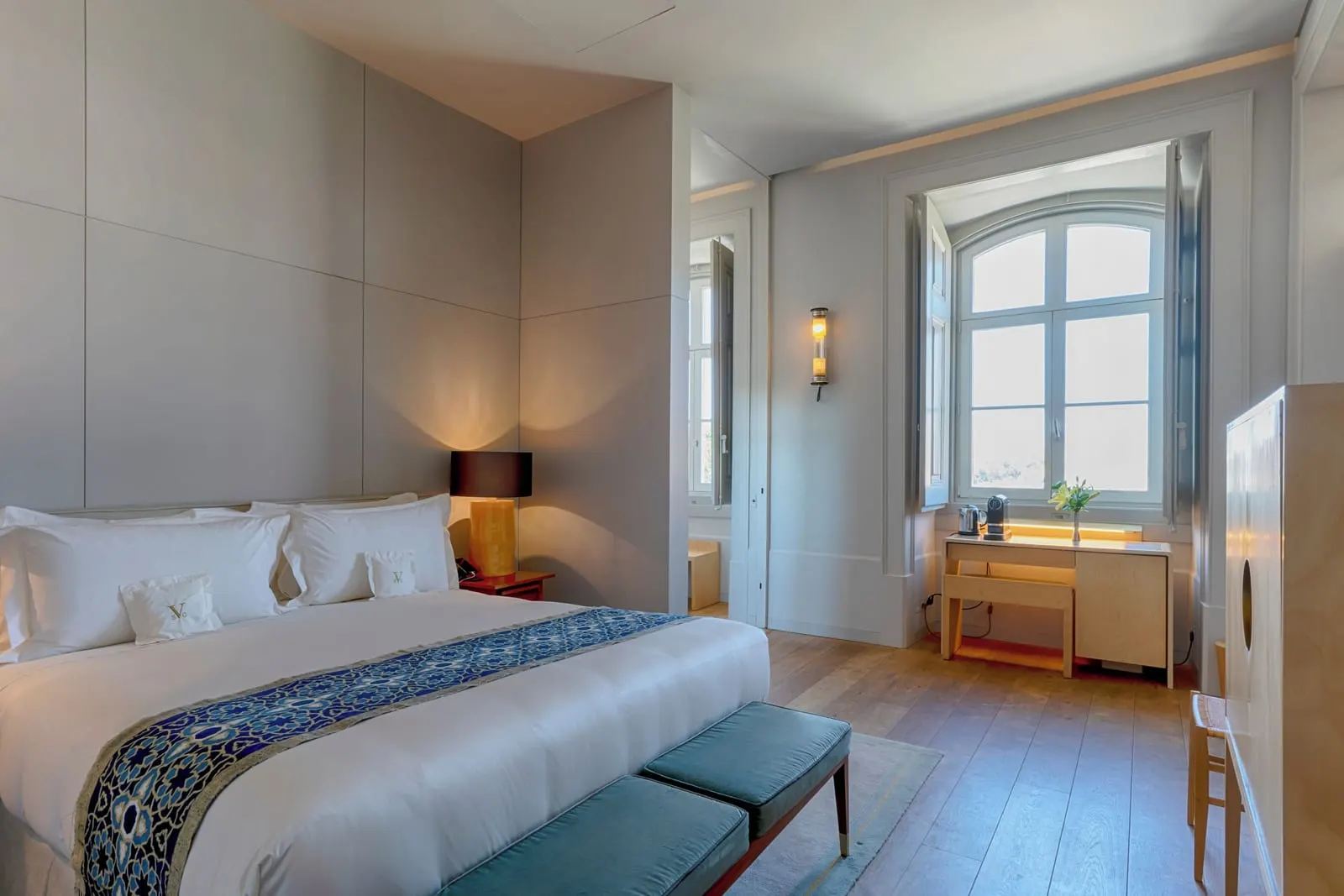 Santa Catarina Superior Room at Verride Palácio Santa Catarina: the bed with a teal bench, and a desk under an arched window