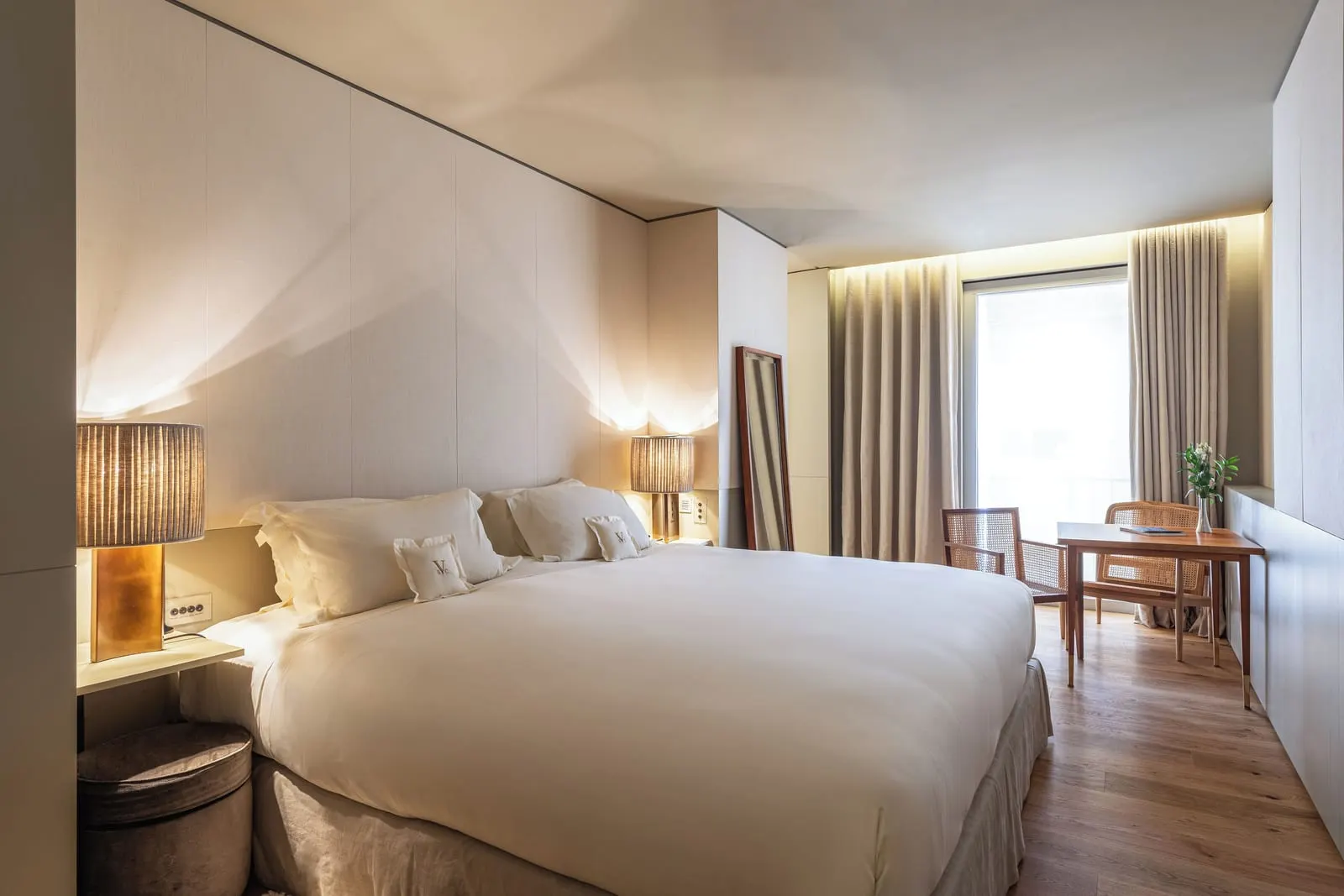 Bica Suite at Verride Palácio Santa Catarina: the bed with lamps either side, and a table with two chairs by a tall window