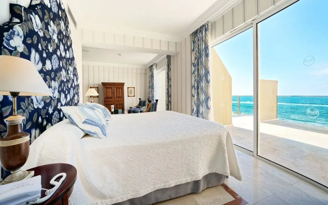 Suite Plus with Sea View at Bull Reina Isabel & Spa: a double bed with a blue floral headboard beside sliding glass doors to a wide balcony and the sea, with a wardrobe and armchairs beyond