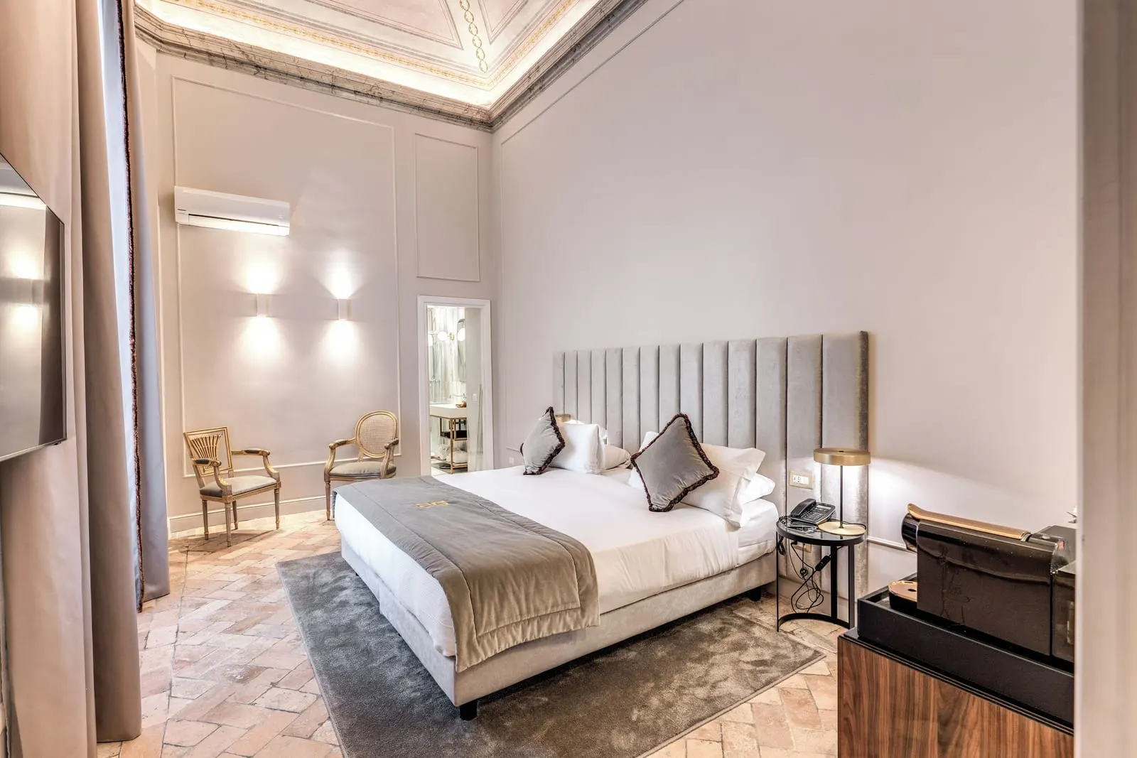 Deluxe Suite at Eitch Borromini Palazzo Pamphilj: a large bed with a tall padded headboard on a terracotta floor
