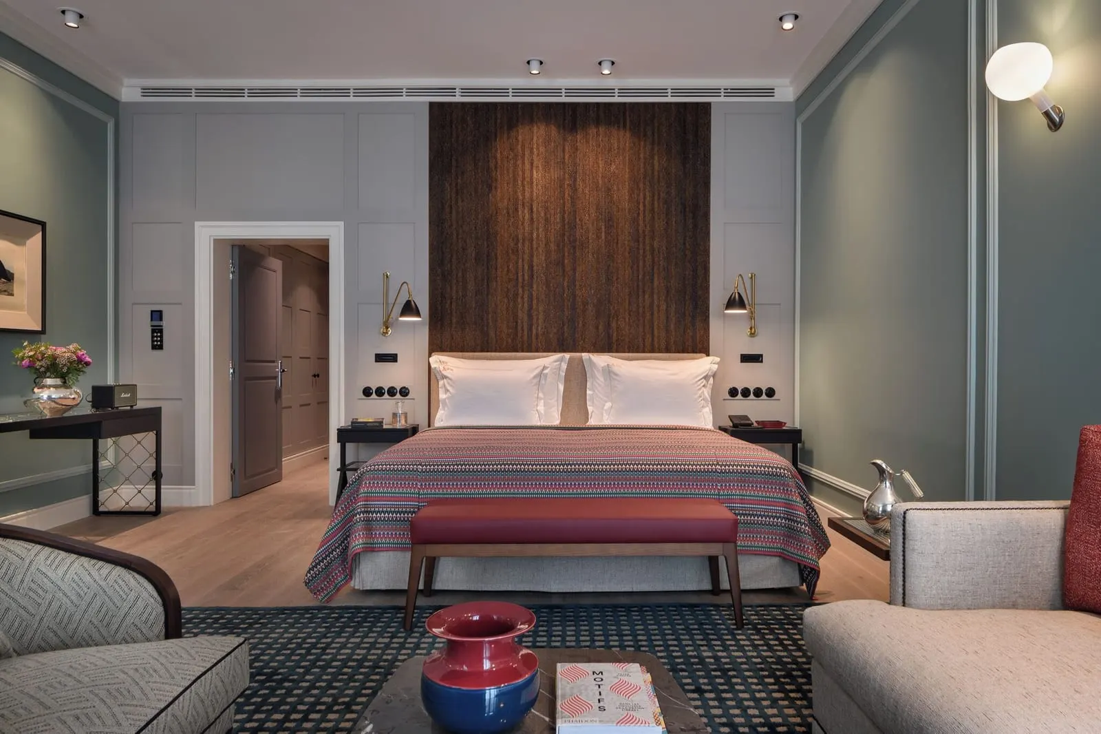 Junior Suite at Bairro Alto Hotel: the bed against a timber panel, with a red bench and sofas in the foreground