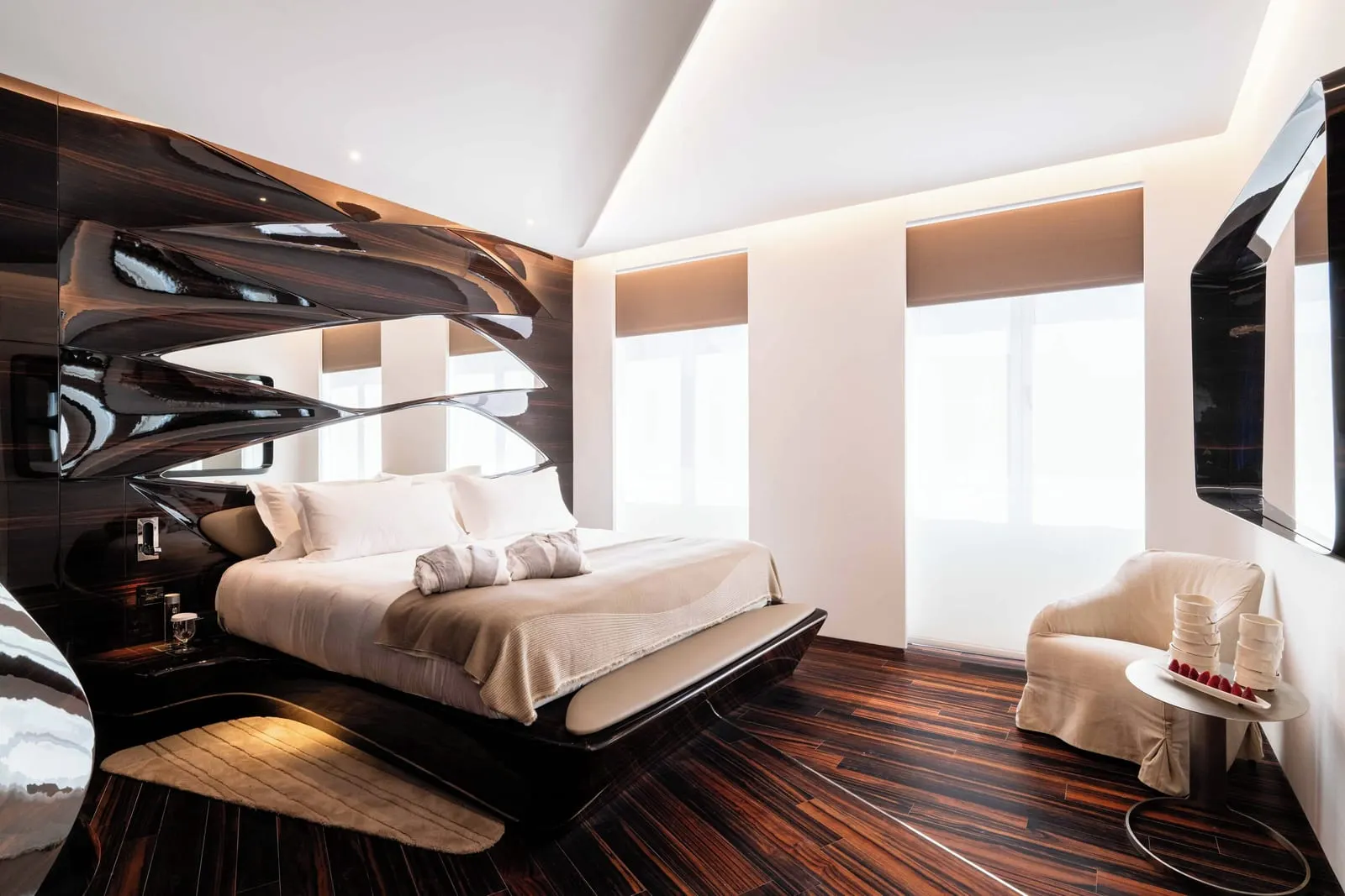 Junior Suite at ROMEO Roma: the bed below a carved ebony headboard, an armchair and two tall windows