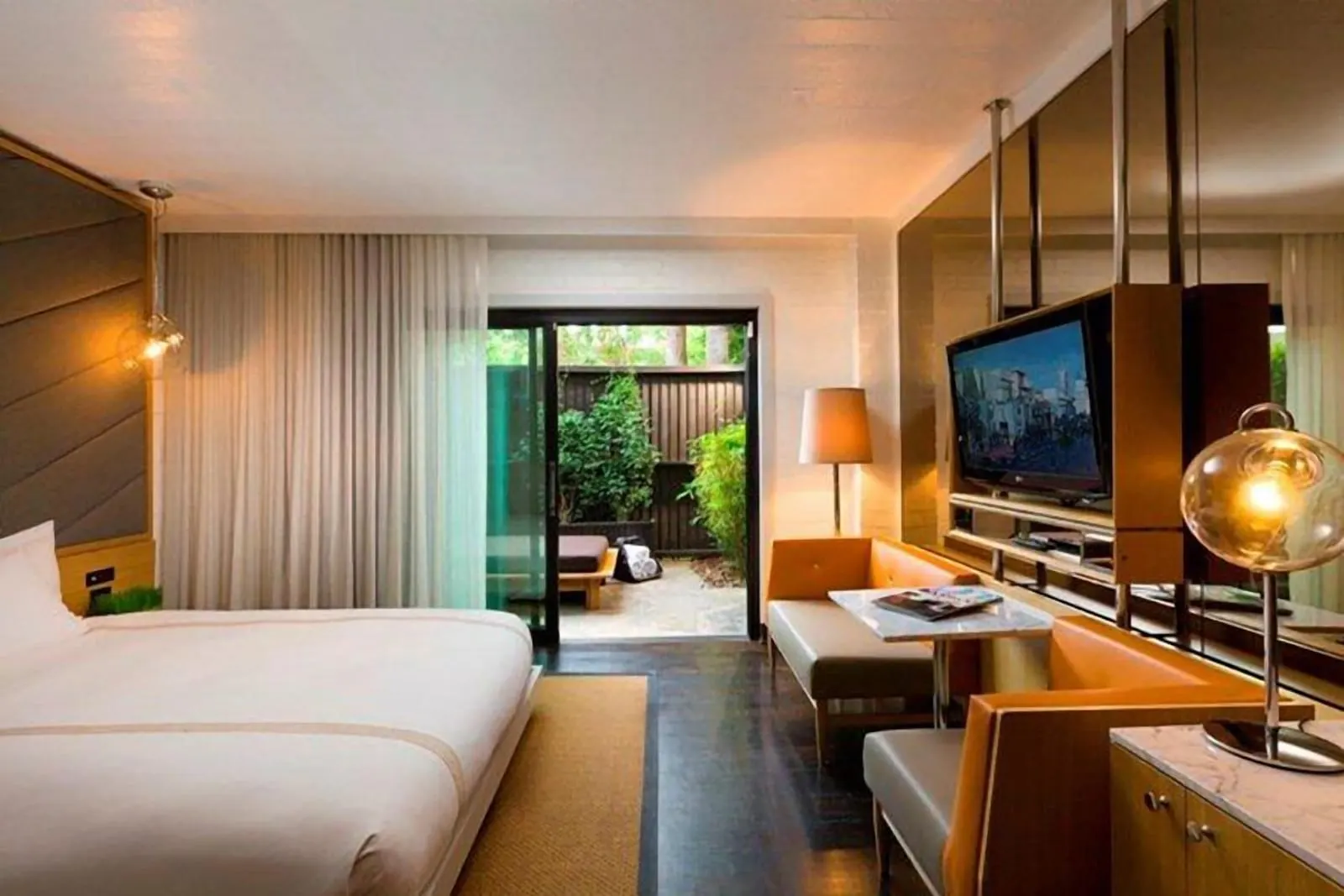 Cabana Garden King im The Hollywood Roosevelt: ein niedriges Bett neben einem drehbaren Fernseher und einer Sitzbank aus Leder, mit gläsernen Schiebetüren zu einem kleinen umzäunten Patio mit einem Tagesbett