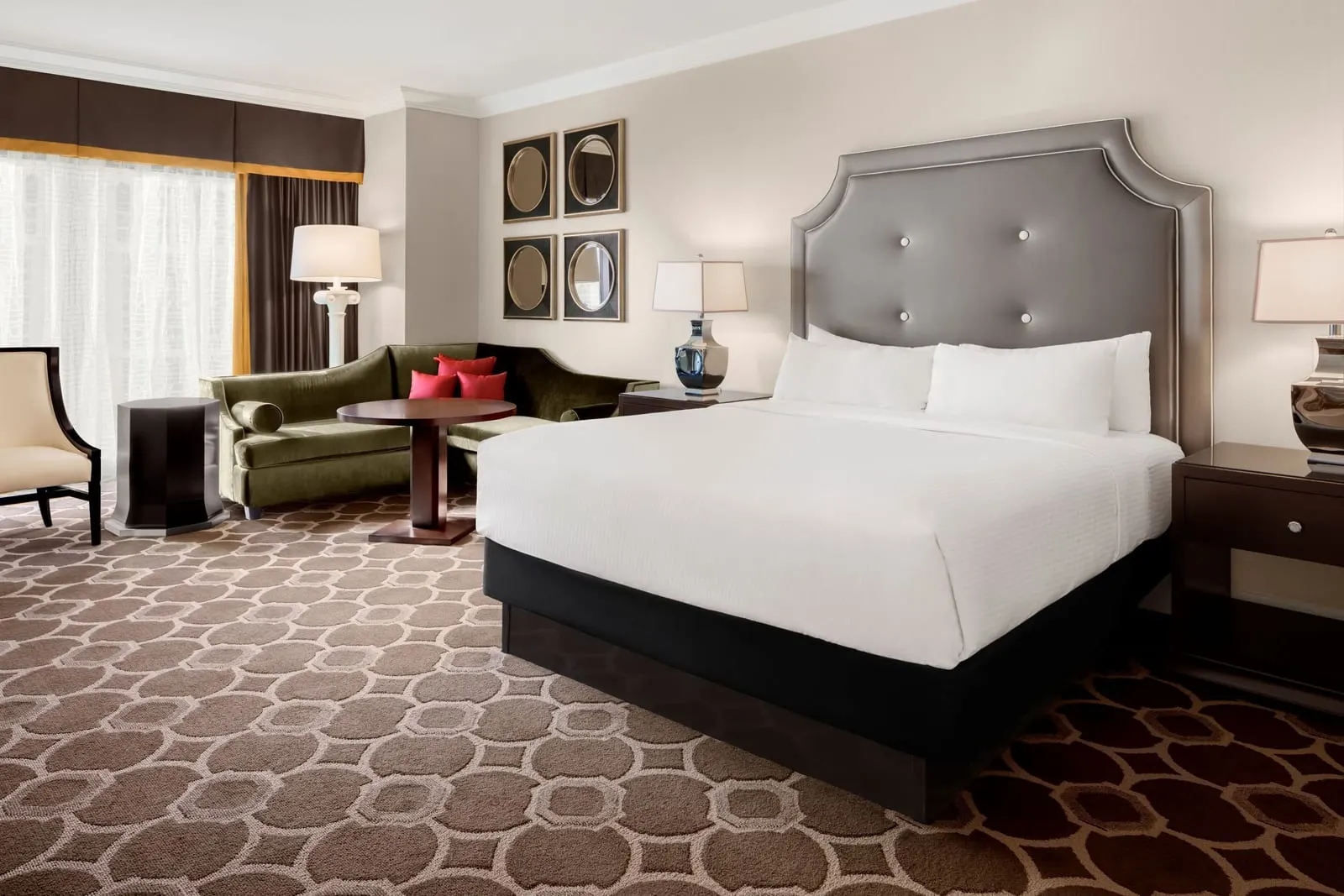 Octavius Premium Room at Caesars Palace: a king bed with a grey tufted headboard, and a green velvet sofa and round table by the window