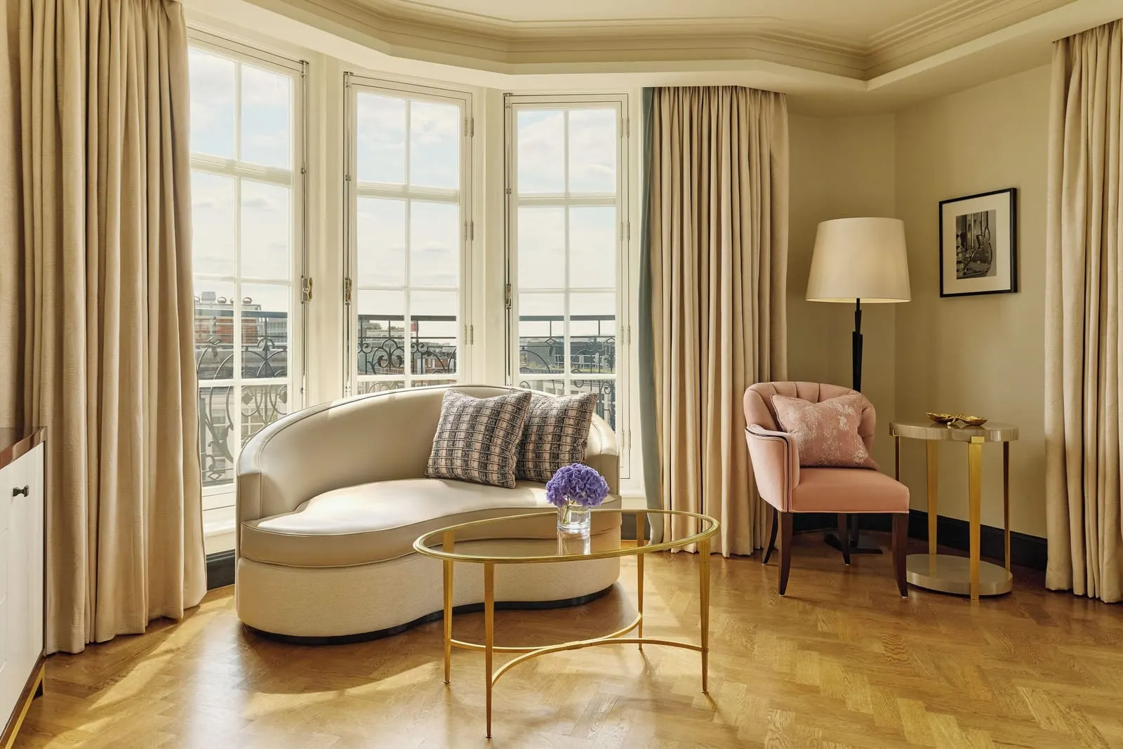 Corner Terrace Suite at Claridge's: a curved sofa, a pink armchair and a glass table by the bay windows