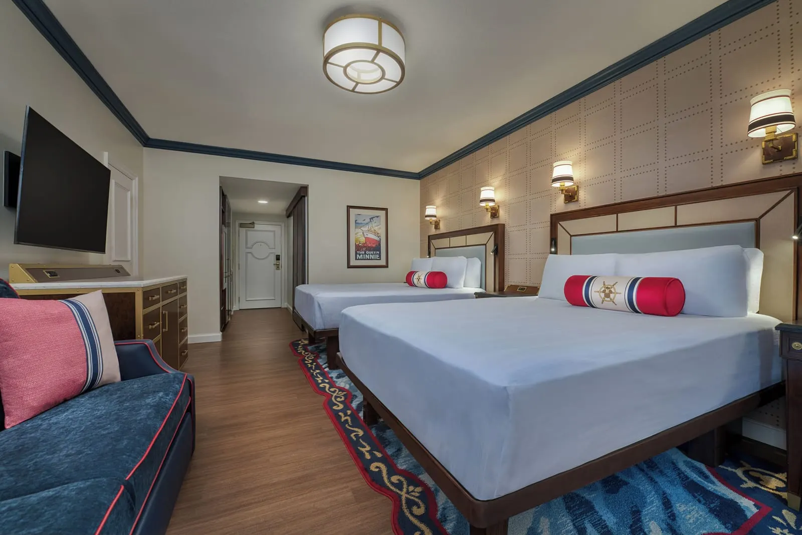 Water View - Club Level room im Disney's Yacht Club Resort: zwei Queensize-Betten, ein marineblaues Sofa, ein Fernseher über der Kommode und der Flur zur Tür