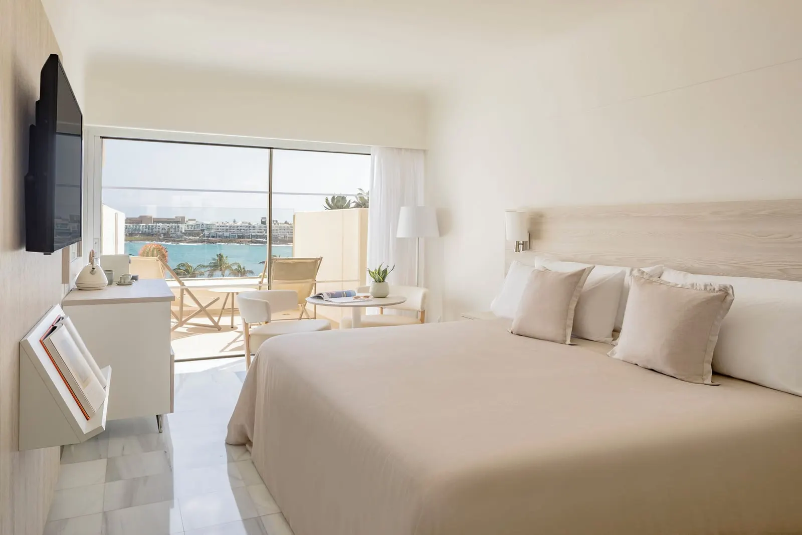 Premium Ocean Front at Paradisus Salinas Lanzarote: a king bed with a television and a terrace with chairs beyond the glass doors