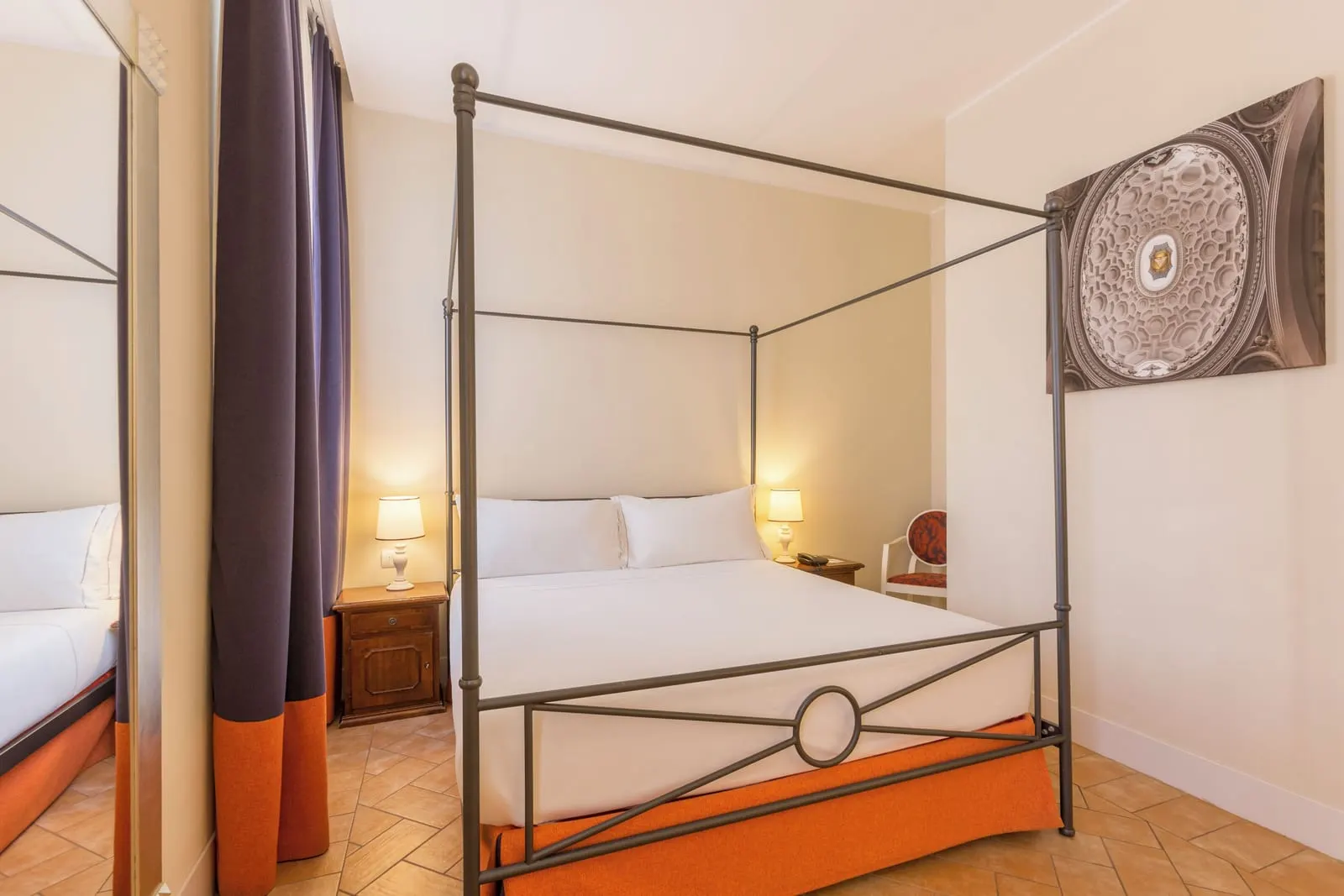 Classic Room at Donna Camilla Savelli: an iron four-poster bed with an orange skirt, bedside lamps and a framed print
