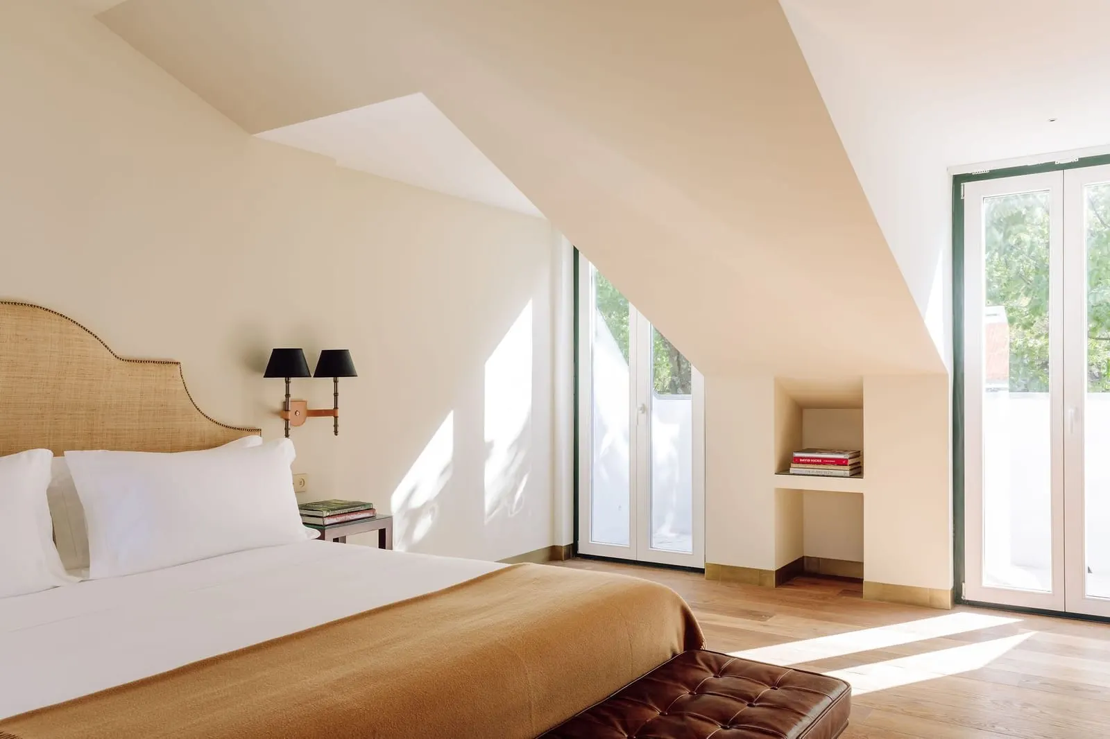 Deluxe Attic Suite at Hotel das Amoreiras: the bed under the sloping roof and two glass doors with trees beyond