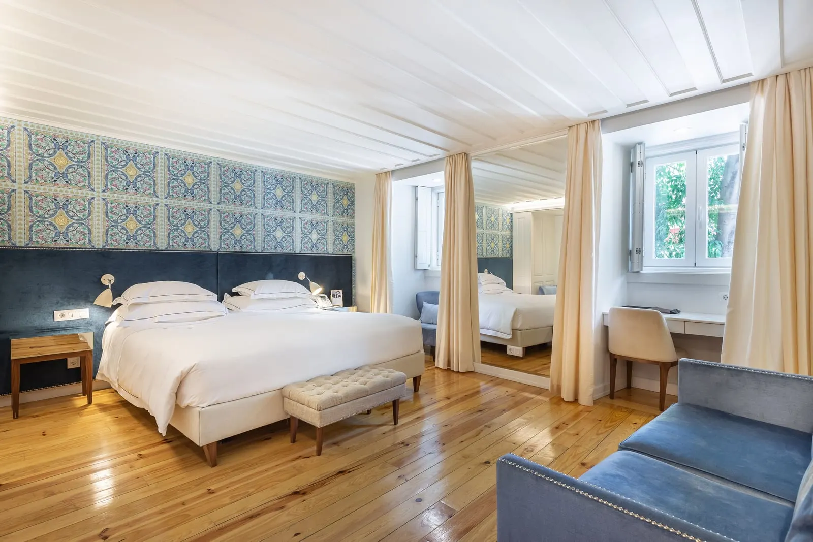 Superior King Bedroom at Santiago de Alfama: the bed against a blue patterned wall, a bench, a desk and a blue sofa