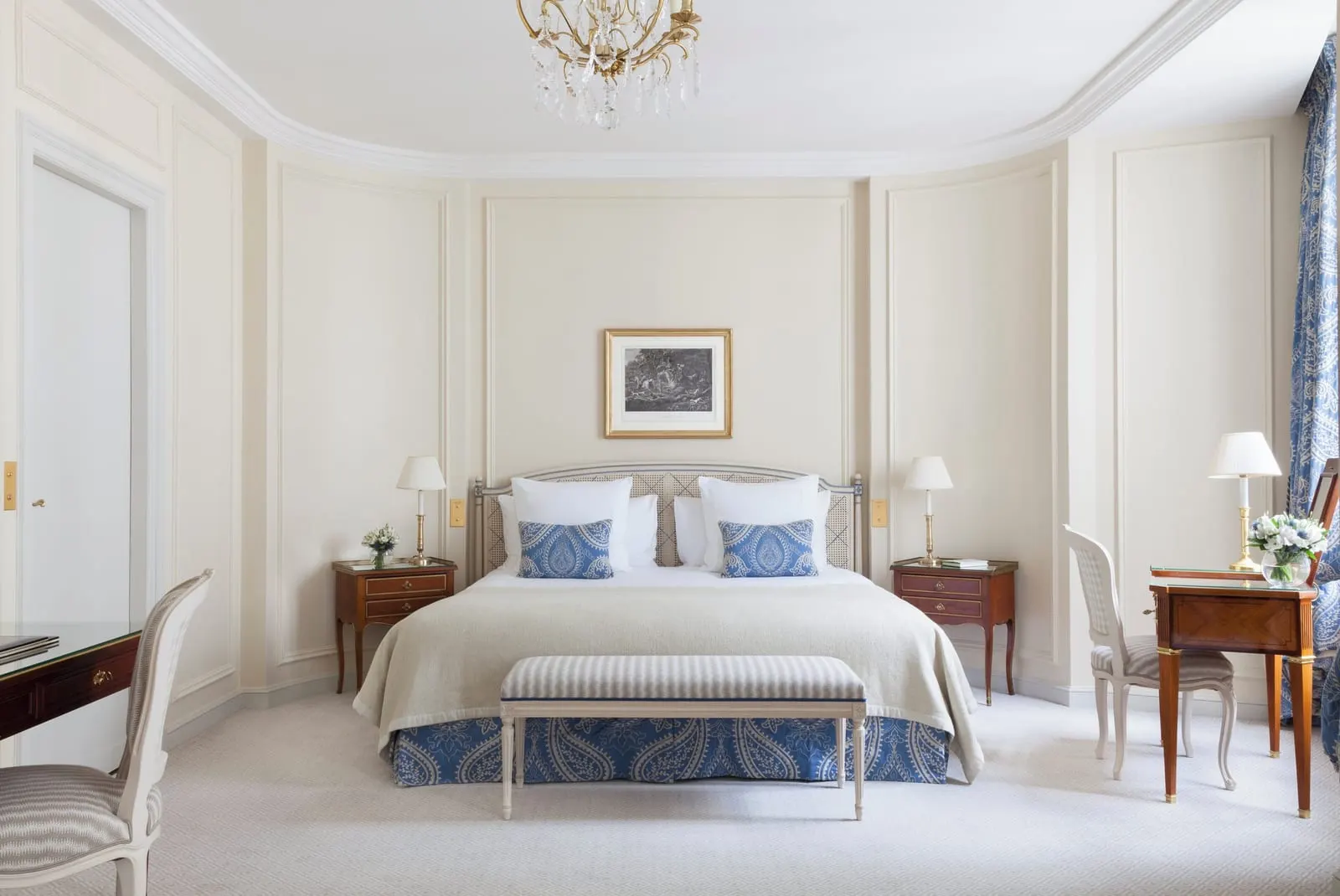 Prestige Room at Le Bristol Paris: a bed with blue paisley cushions and a striped bench at its foot between two bedside tables, with a writing desk to one side