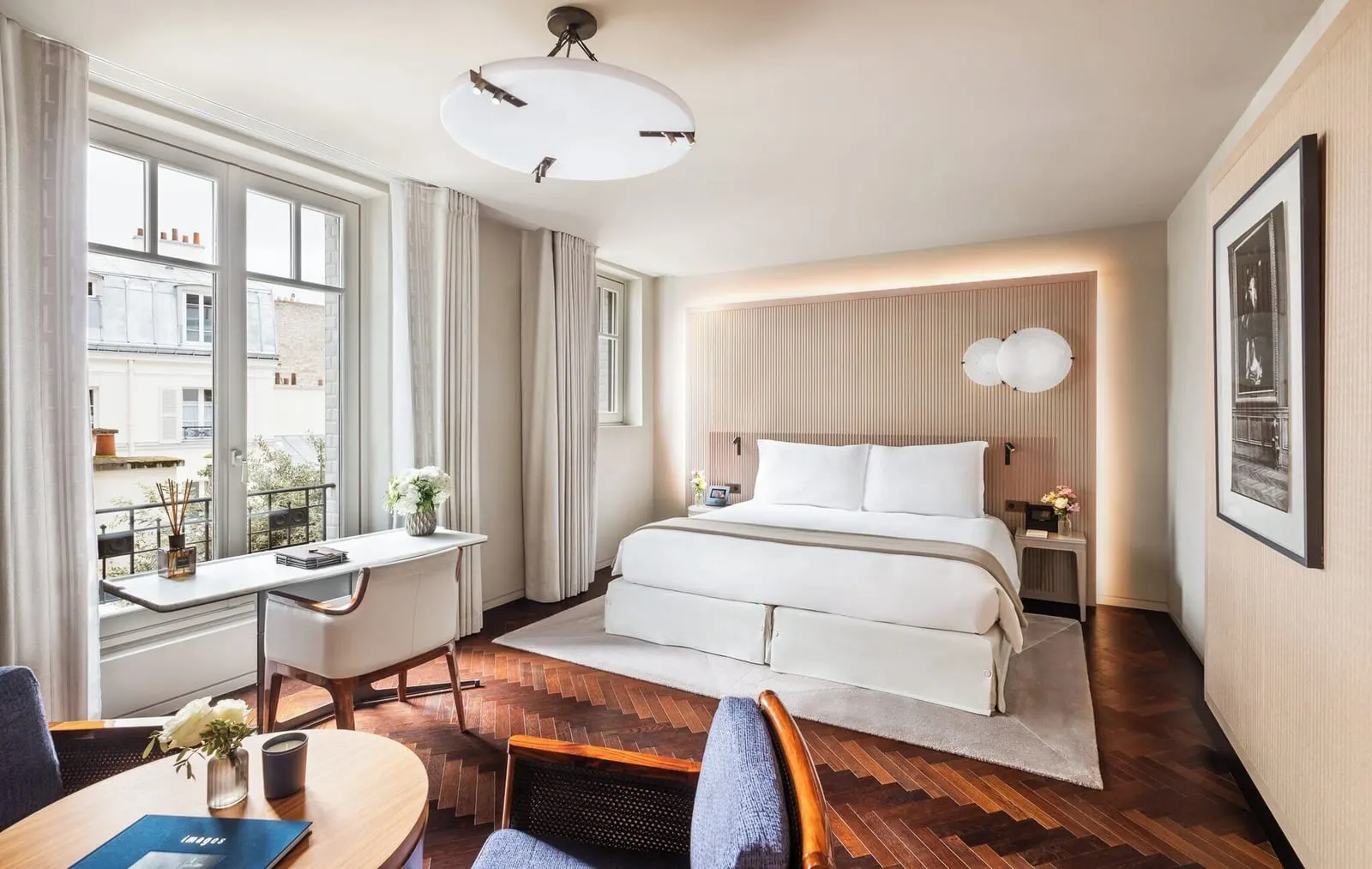 Deluxe Room at Mandarin Oriental Lutetia, Paris: a double bed against a pale fluted headboard, a writing desk under tall windows, a round table with two blue armchairs and a herringbone wood floor