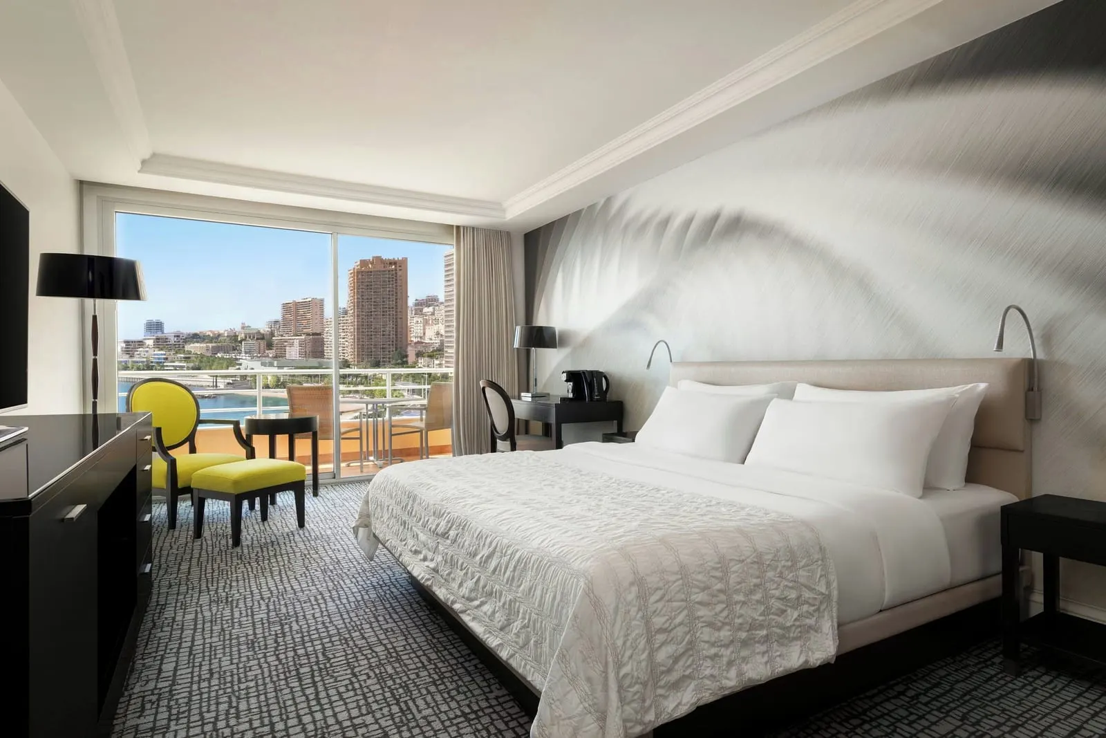 Deluxe room with partial sea view at Le Méridien Beach Plaza: the bed, a yellow armchair and a window onto towers and the sea