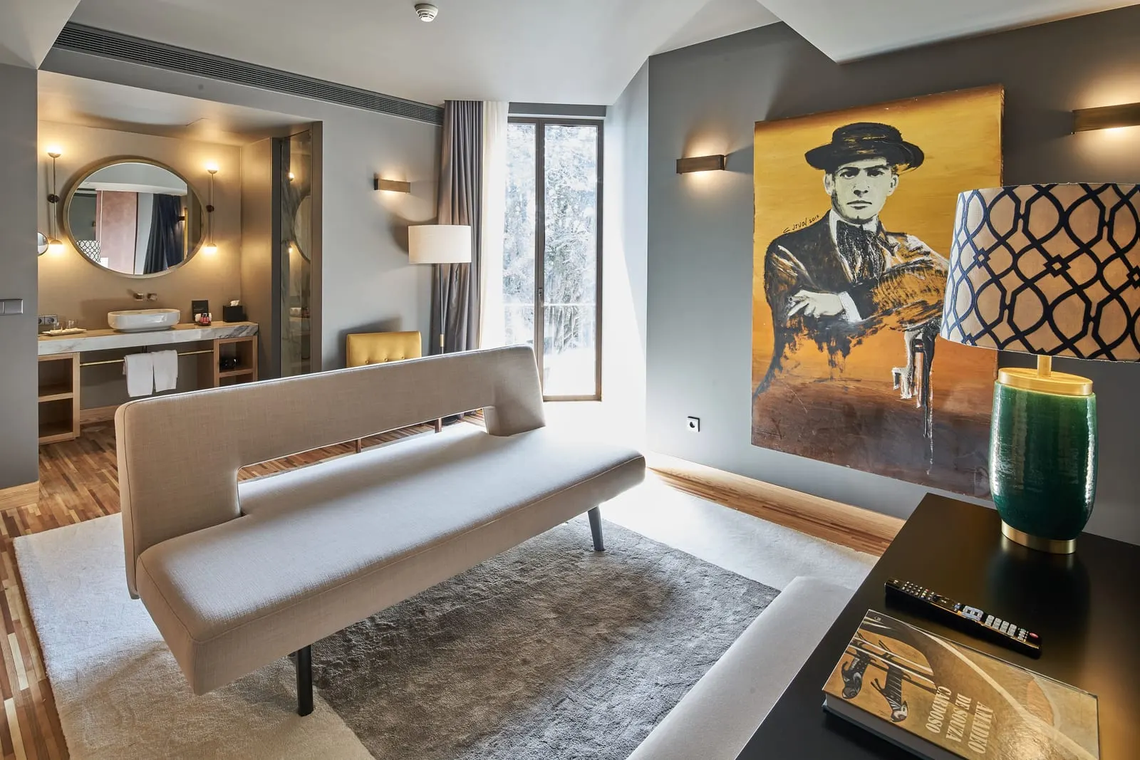 Suite at Torel Avantgarde: a sofa, a desk and a large portrait painting, with the washbasin and a round mirror beyond