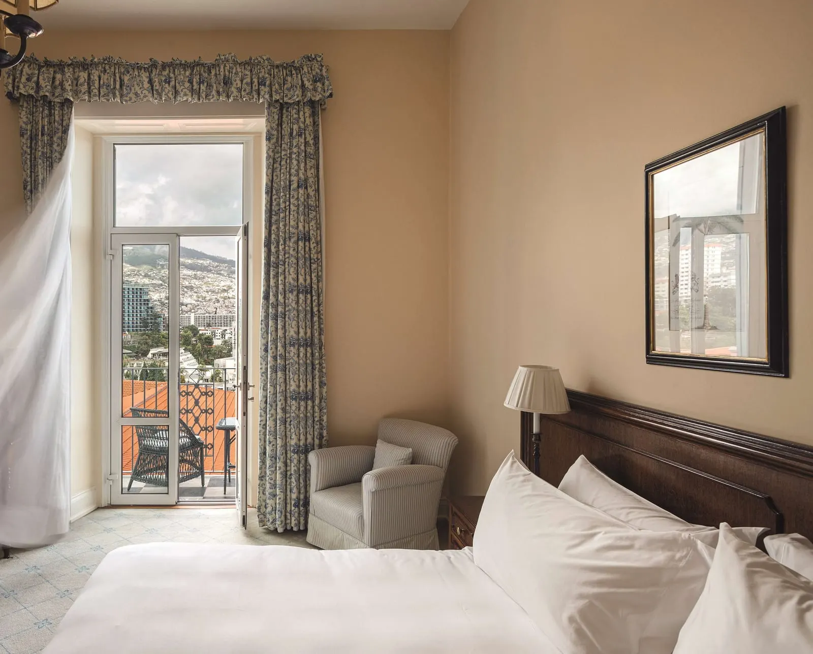 Deluxe Sea View Room at Reid's Palace, A Belmond Hotel: the bed and an armchair beside open doors to a furnished balcony