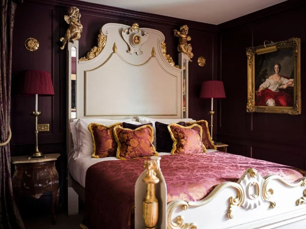Junior Suite al Hazlitt's: un letto intagliato e ornato, bianco e dorato, con cuscini rossi, su pareti rivestite in legno scuro