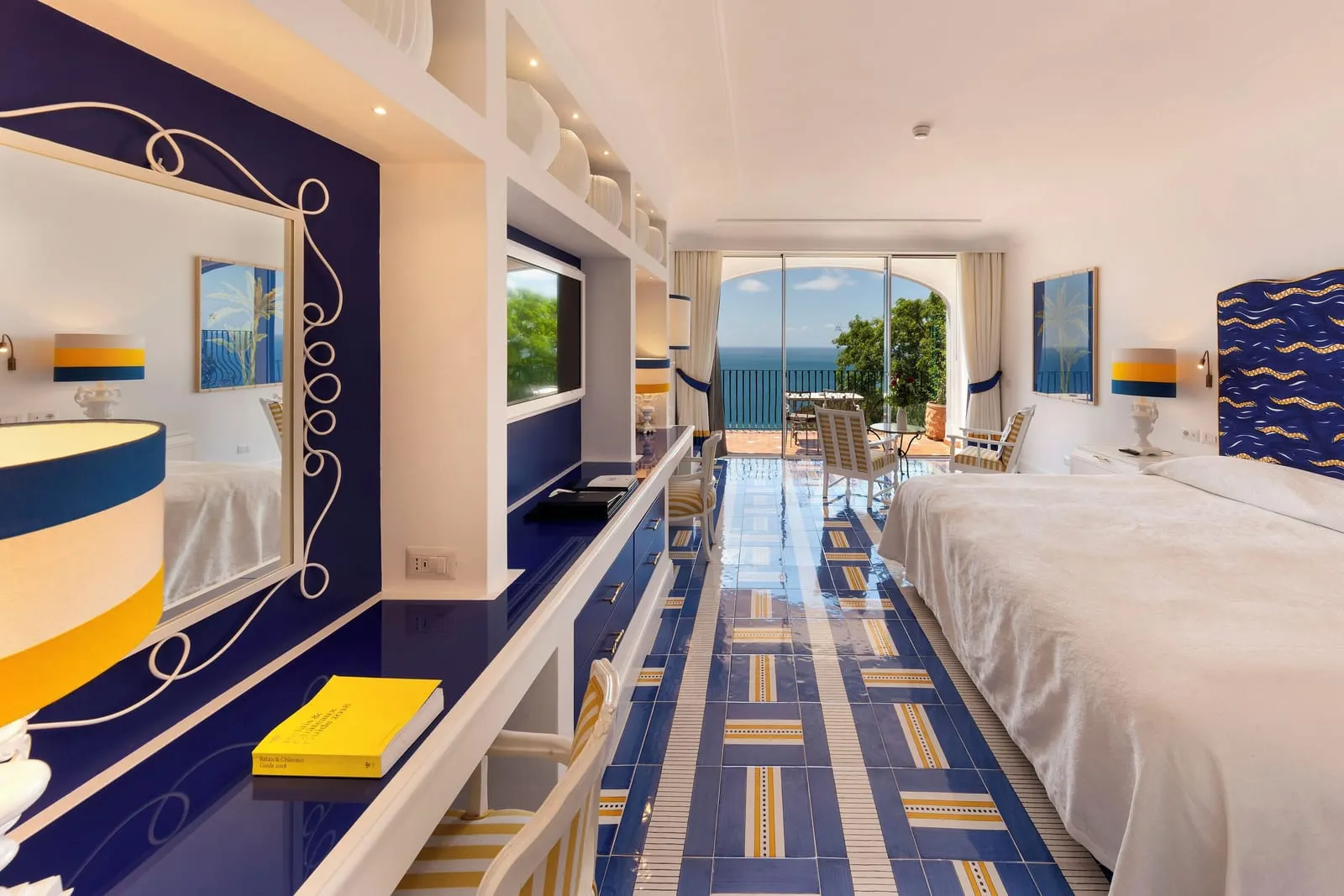 Premier Room at Il San Pietro di Positano: a long room with a large bed on blue and yellow tiles, leading to a terrace with sunbeds over the sea