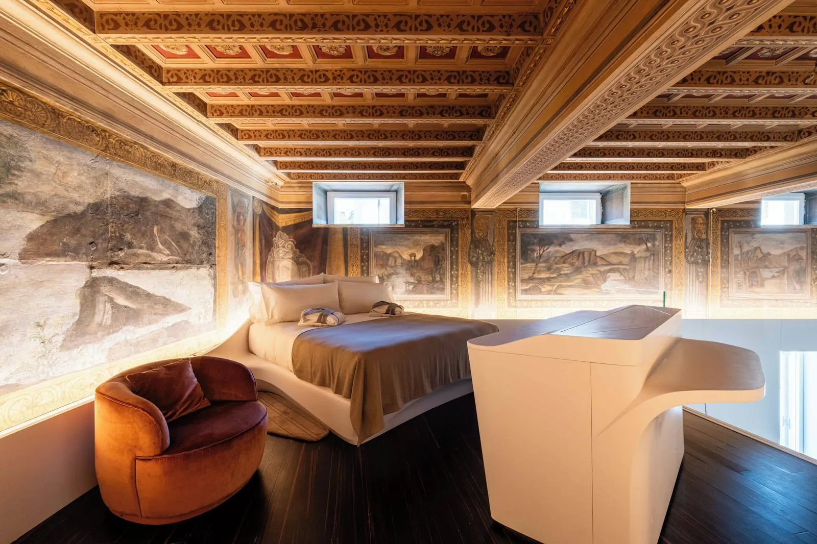 Fresco Suite at ROMEO Roma: a bed on the mezzanine under a coffered ceiling and frescoed walls, a velvet armchair in front