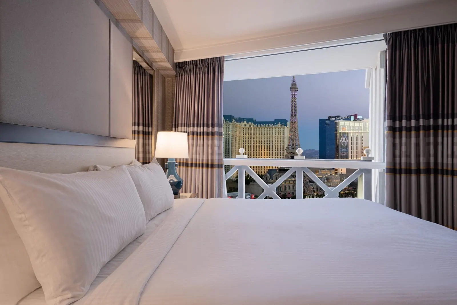Julius Corner Studio Suite im Caesars Palace: ein Kingsize-Bett neben einem hohen Fenster mit Blick auf den Strip und den Turm des Paris Las Vegas