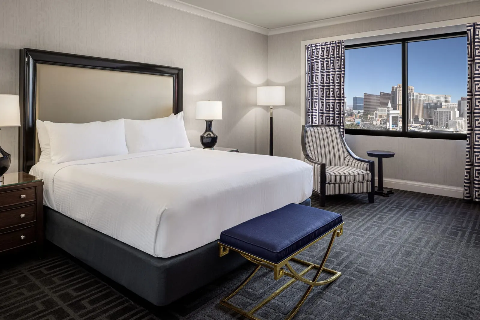 Palace Premium Studio Suite im Caesars Palace: ein Kingsize-Bett mit einer blauen Bank am Fußende, ein gestreifter Sessel und ein Beistelltisch an einem breiten Fenster