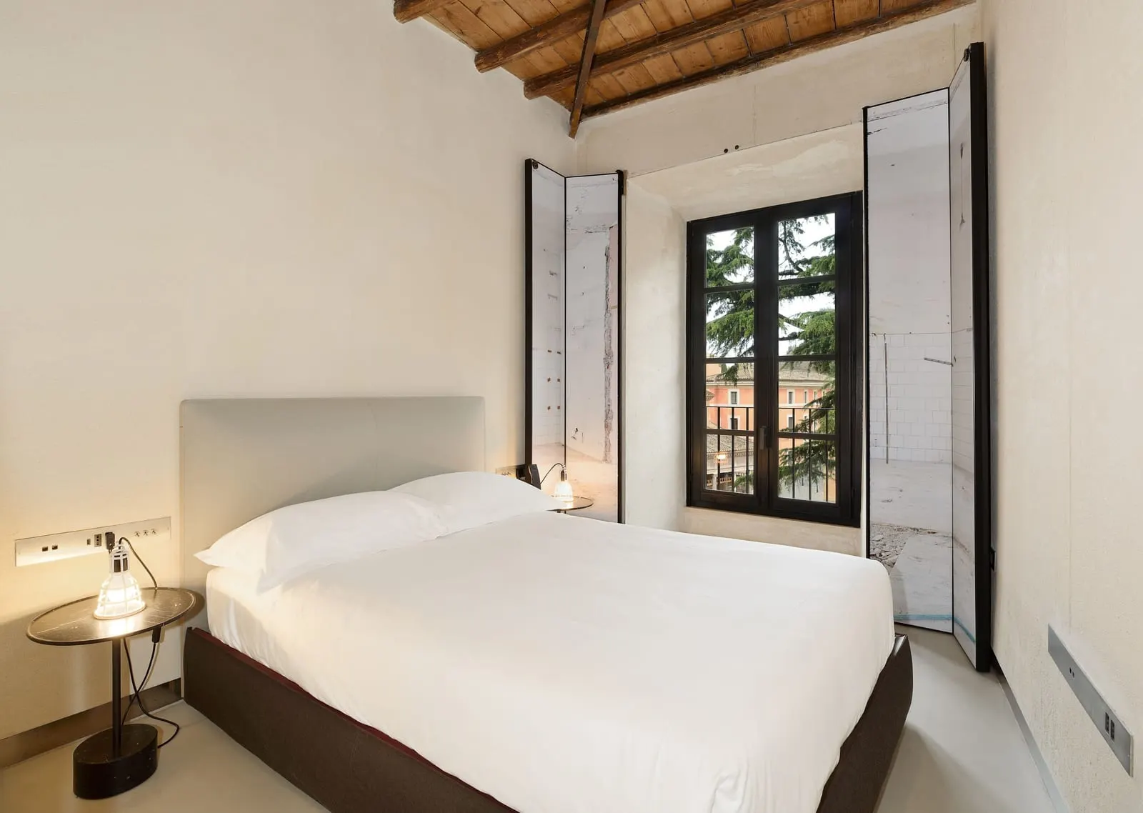 Deluxe Single Apartment at Rhinoceros Roma: a bed with a grey headboard beside a tall window with open shutters