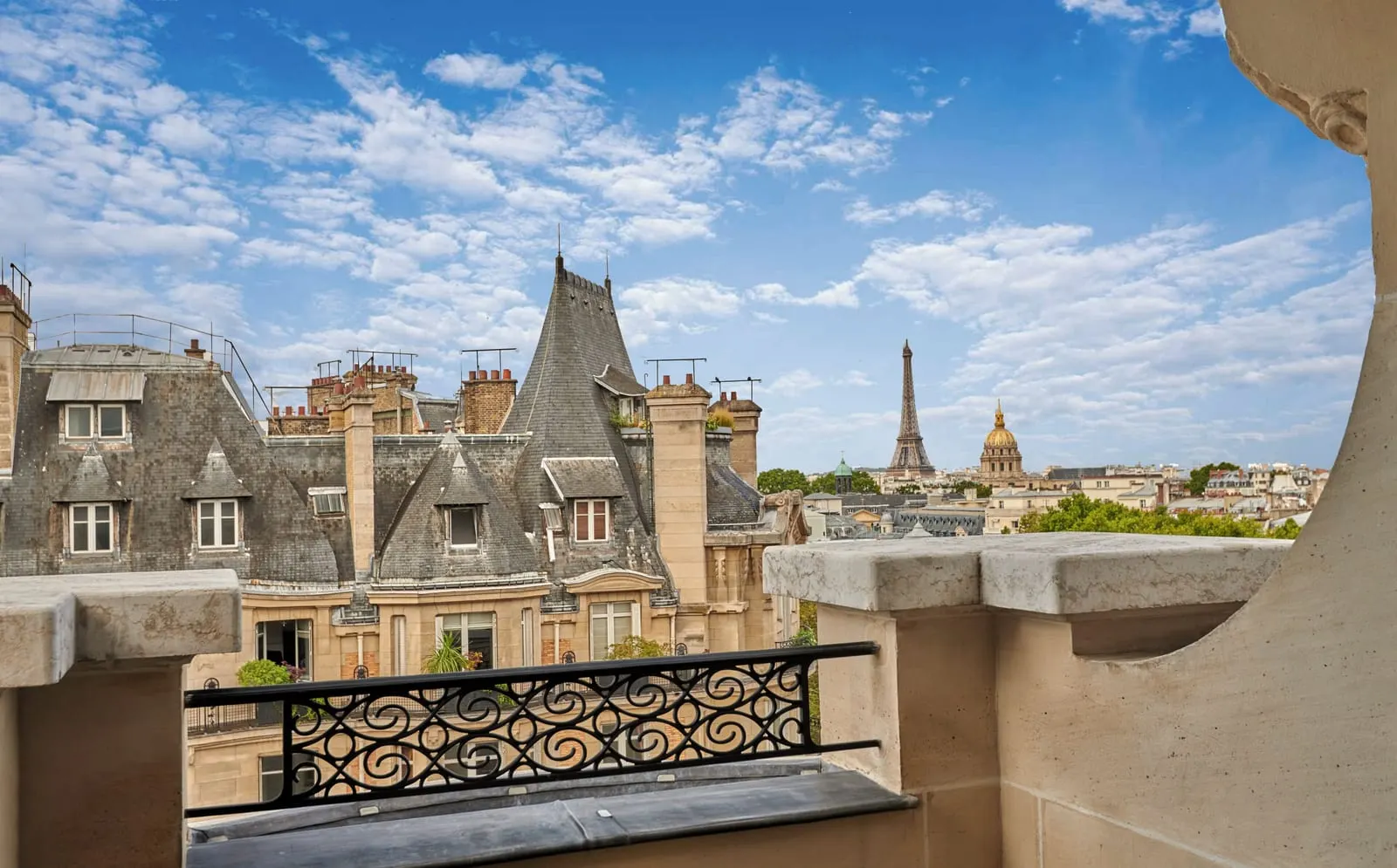 Eiffel View Deluxe Balcony Room at Mandarin Oriental Lutetia, Paris: the balcony's stone ledge and wrought-iron rail, looking over slate rooftops to the Eiffel Tower with the gilded dome of Les Invalides to its right