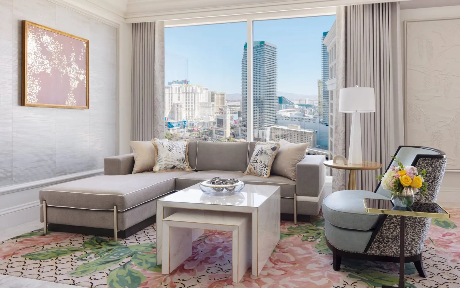 Two Bedroom Penthouse Suite at Bellagio: the living room, with an L-shaped sofa, a white coffee table and an armchair by a tall window onto the Las Vegas skyline