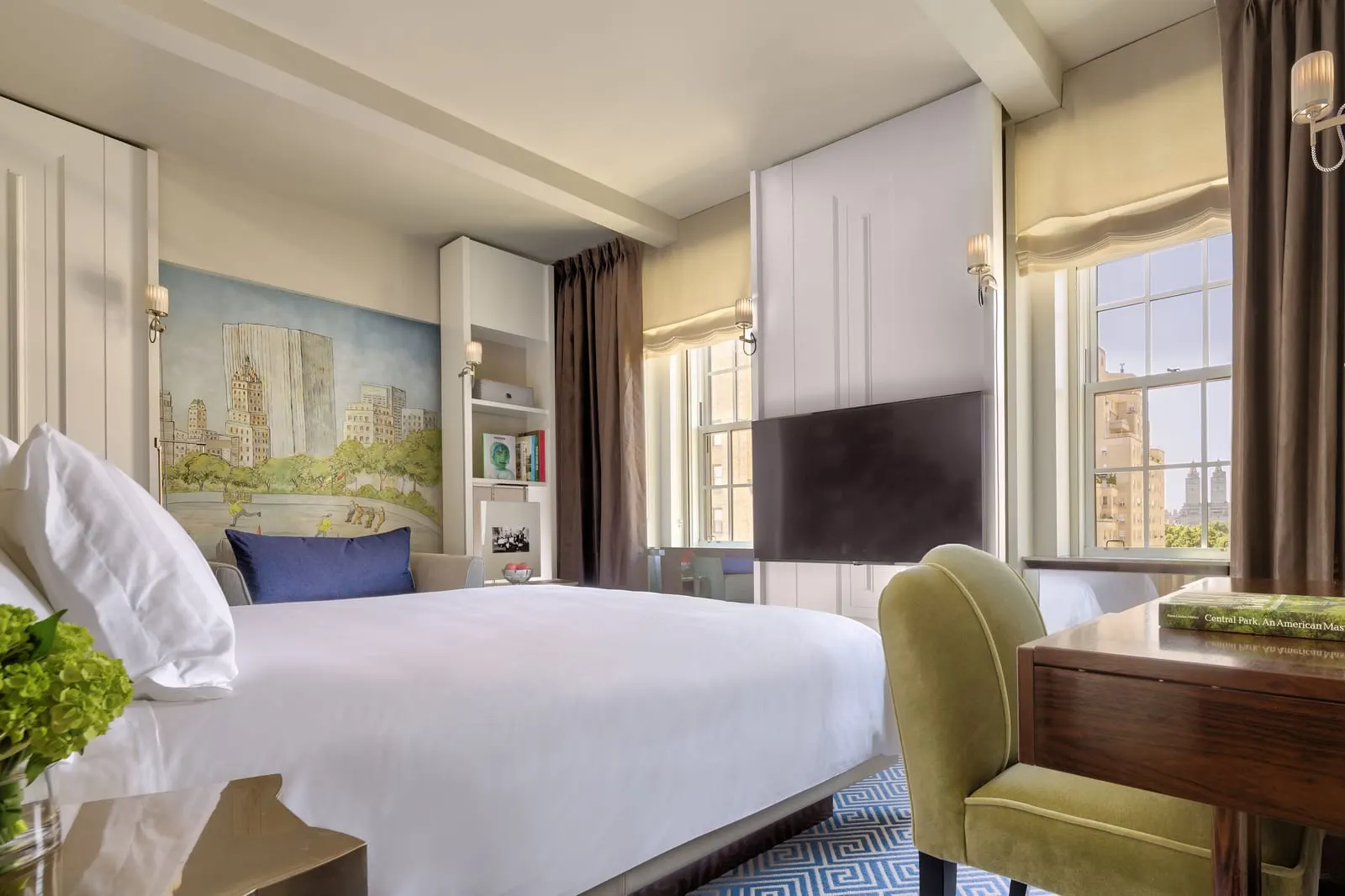 Madison Room at The Carlyle: a king bed beside a painted mural, with a green velvet desk chair and two tall windows