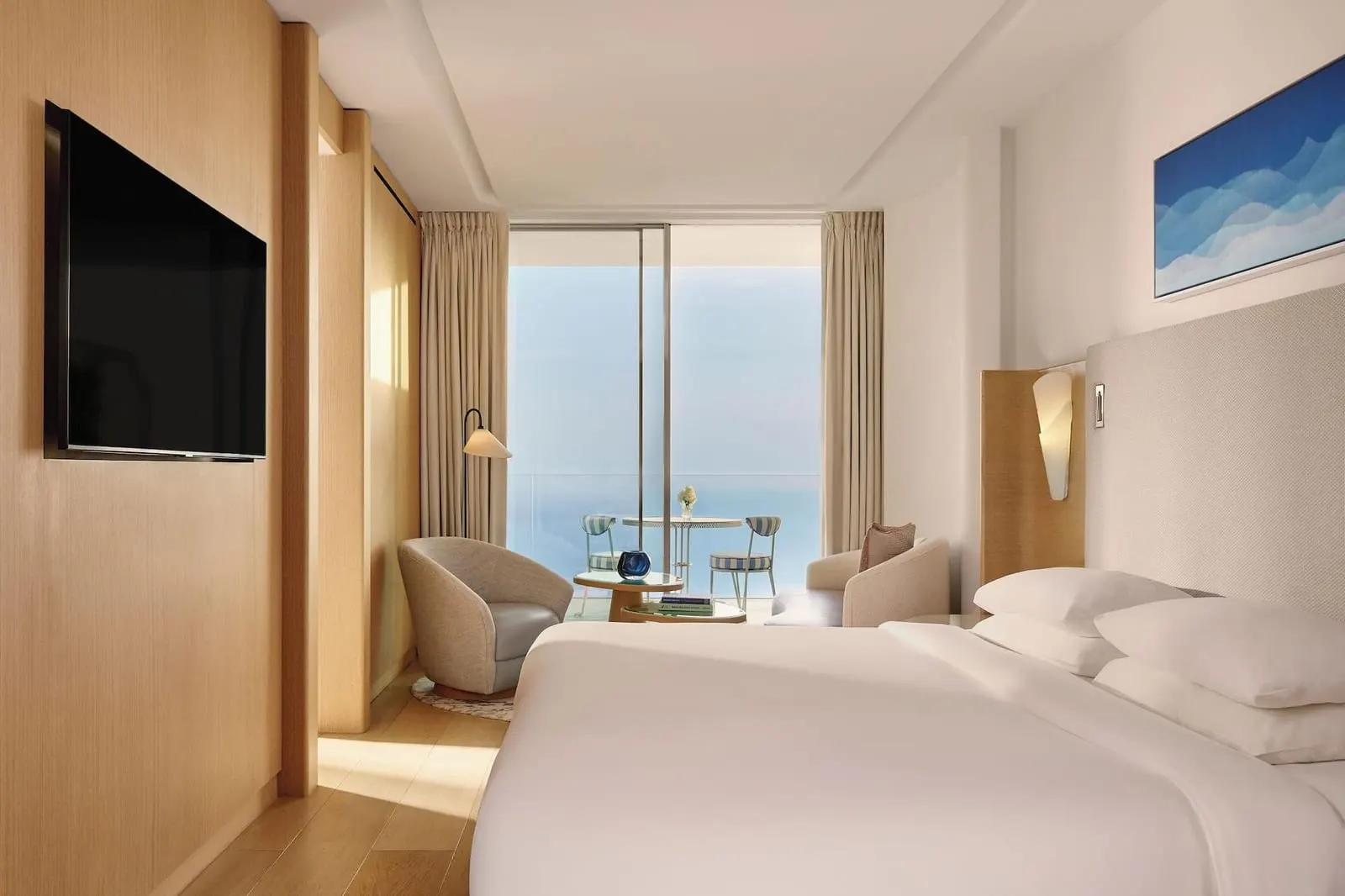 Sea View Studio at The Maybourne Riviera: the bed, a wall-mounted television and two armchairs by a window onto the sea