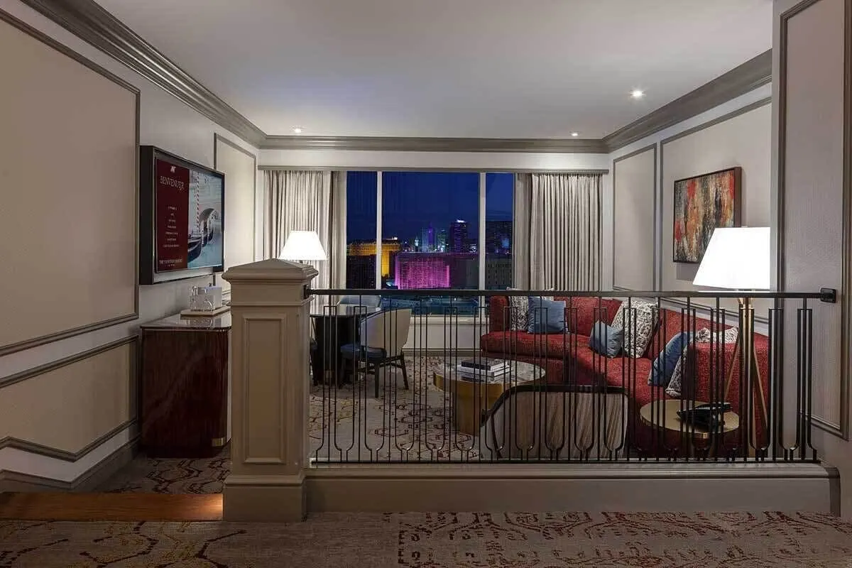 Newly Remodeled Luxury King Suite, Strip View, at The Venetian: the living area at night, seen over a railing, with a red sofa, a round coffee table and a dining table with chairs