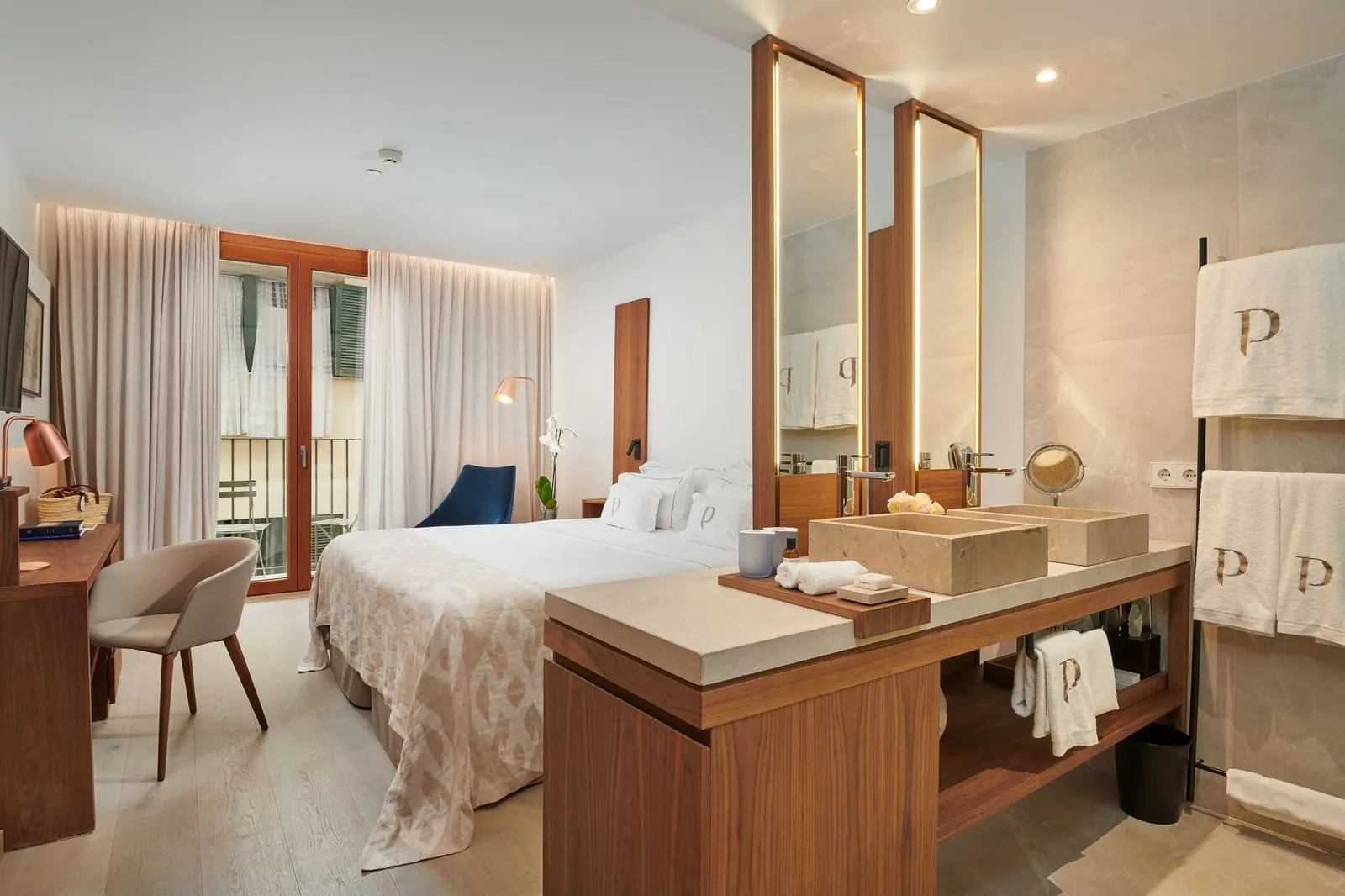 Standard at Es Princep: a double bed beside an open washbasin of pale stone, with a balcony door looking across a narrow street