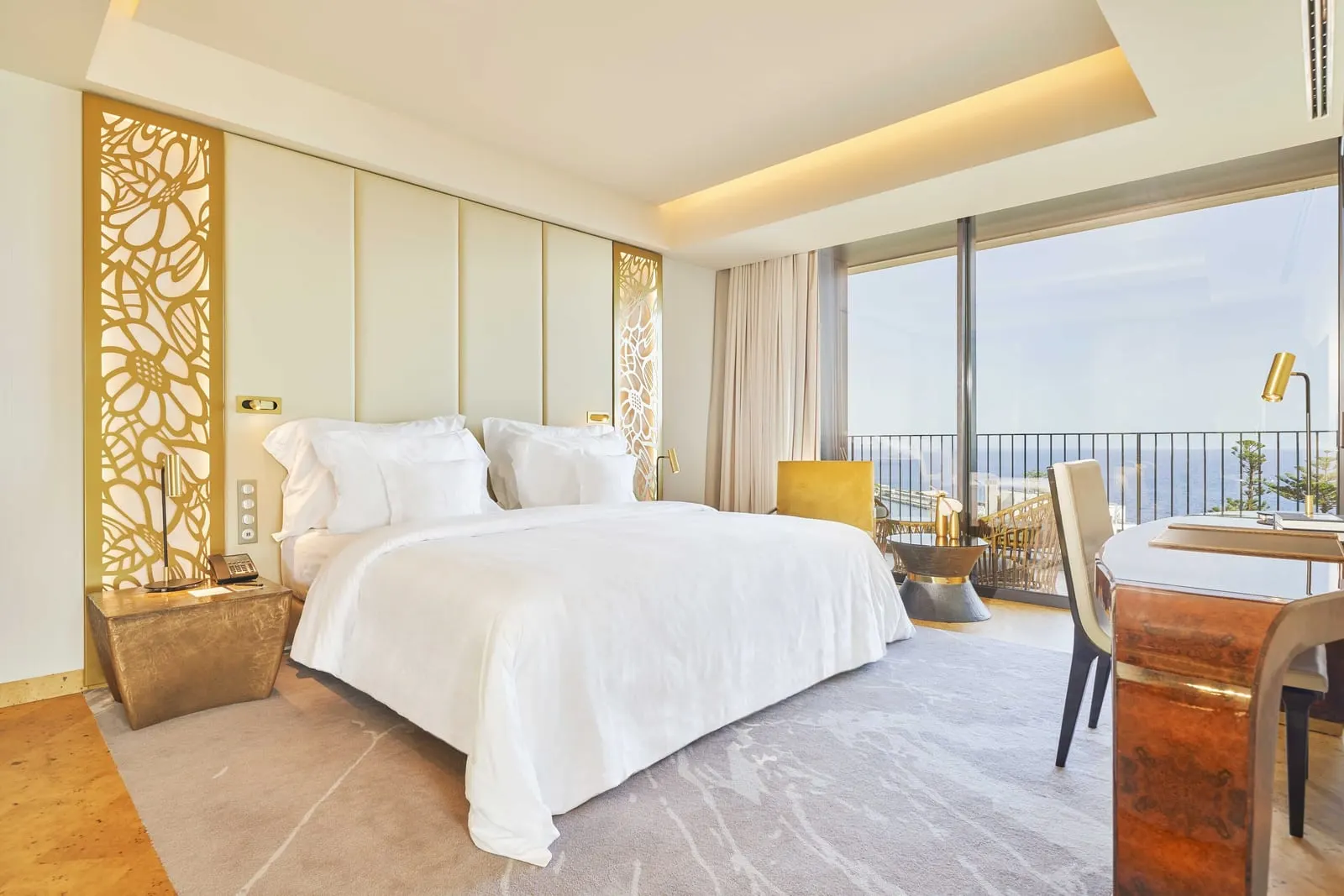 Ocean Suite im Savoy Palace: ein Kingsize-Bett zwischen goldenen Gitterpaneelen, mit einem Schreibtisch und einem raumhohen Fenster zu einem Balkon und dem Meer