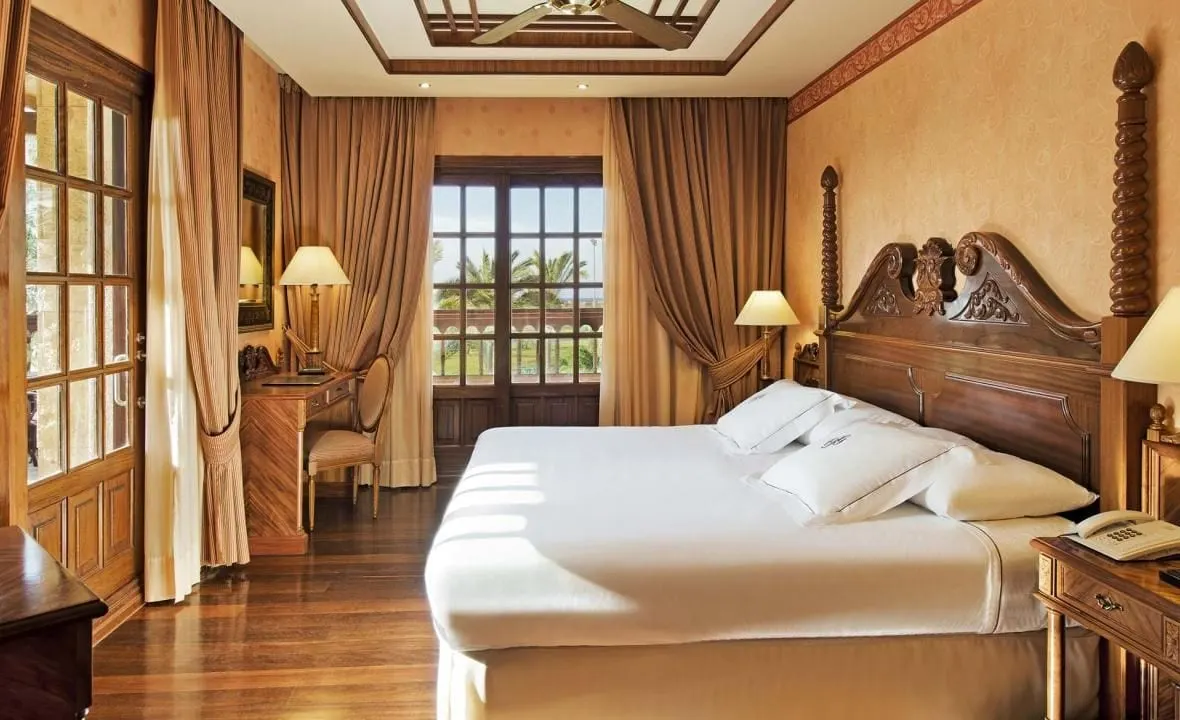Standard Suite at Elba Palace Golf Boutique Hotel: a king bed with a carved wooden headboard, a writing desk and two sets of glazed doors