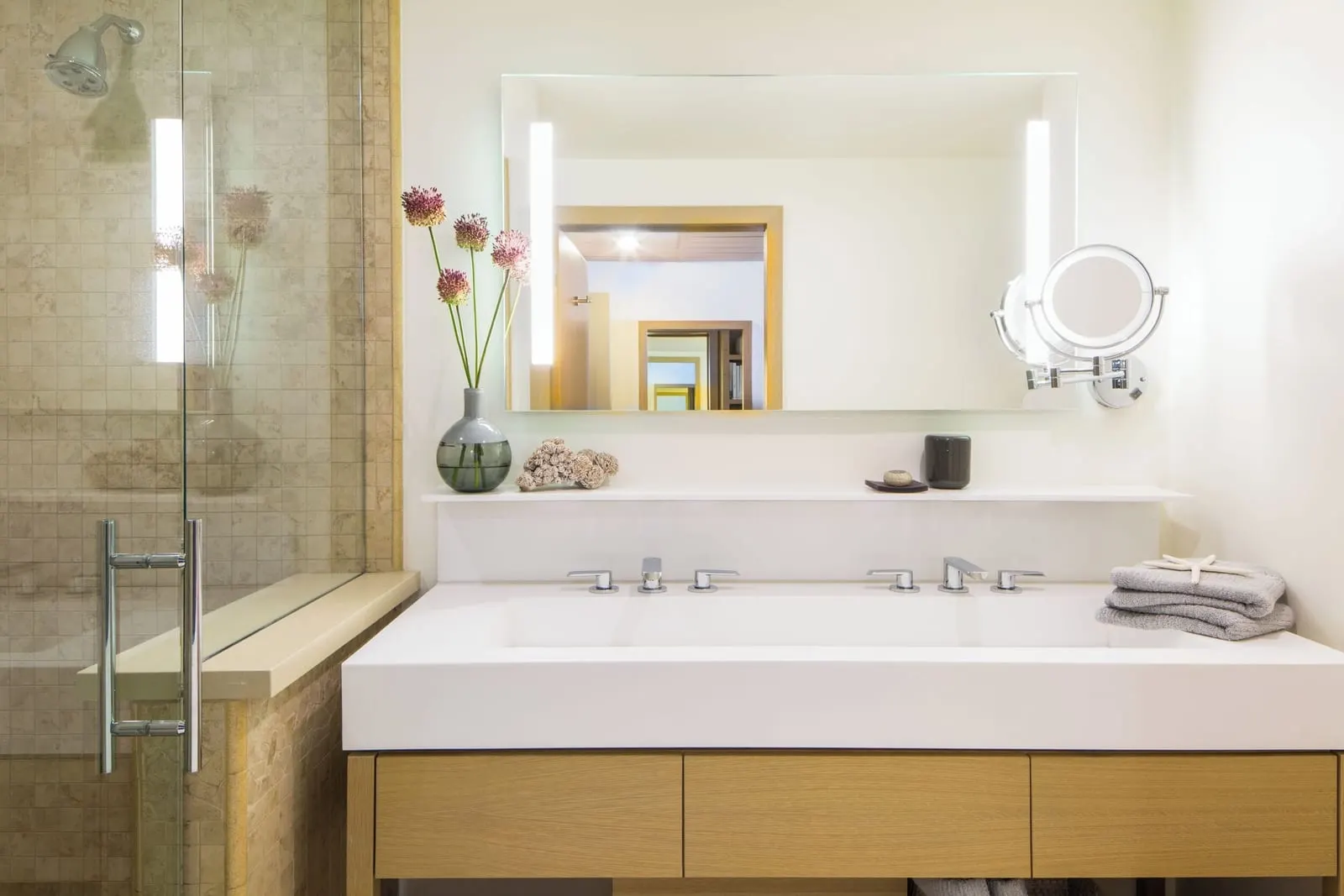 King Premier Ocean Front Room at Malibu Beach Inn: a bathroom with a long white vanity, a lit mirror and a glass-fronted shower