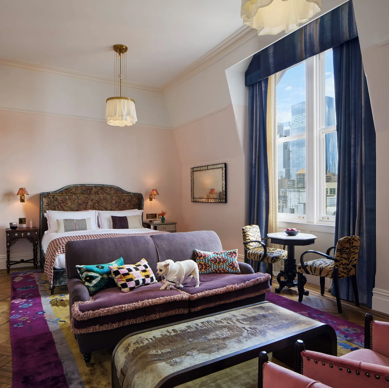 Chelsea Loft at Hotel Chelsea: a bed with a velvet headboard, a purple sofa at its foot and a tiger-print chair and table by a tall window, with skyscrapers beyond