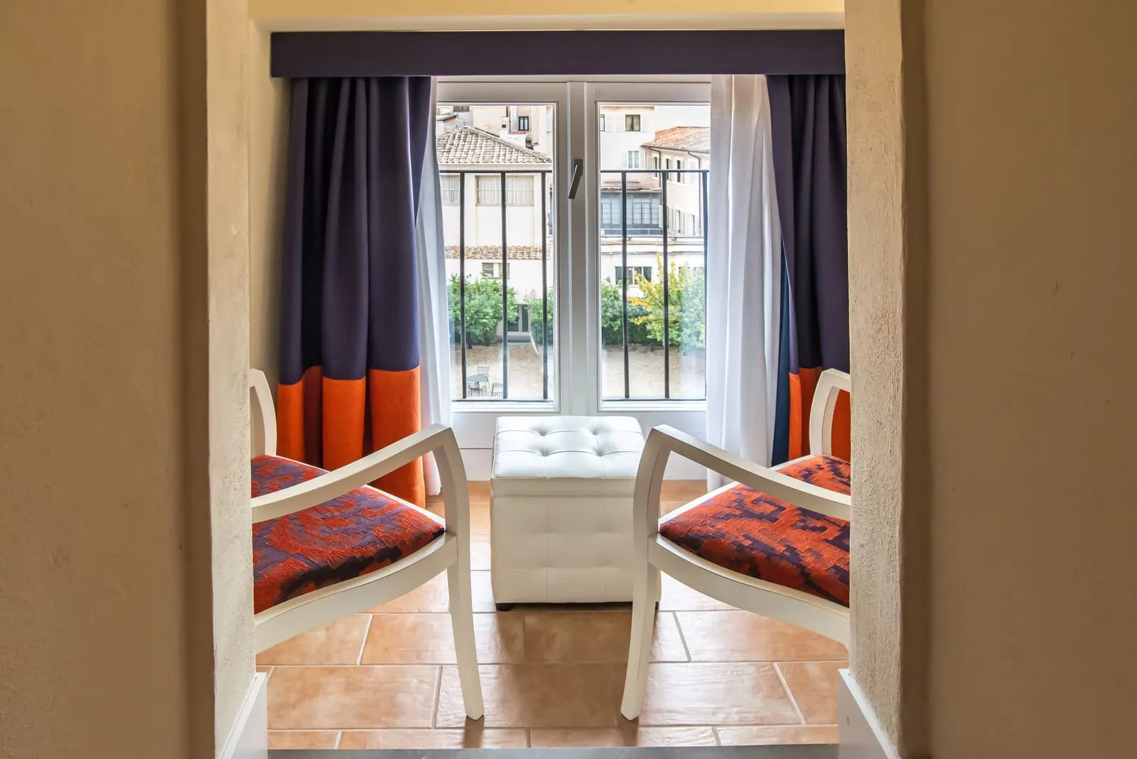 Classic Family at Donna Camilla Savelli: two upholstered chairs and a footstool at a window with navy and orange curtains