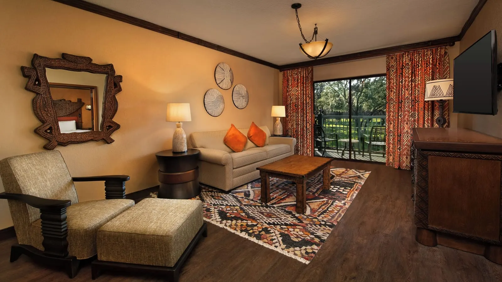 Resort View 1 Bedroom Club Level Suite at Disney's Animal Kingdom Lodge: the living room, with a sofa, a wooden coffee table on a patterned rug, an armchair and footstool, and a glass door onto the balcony
