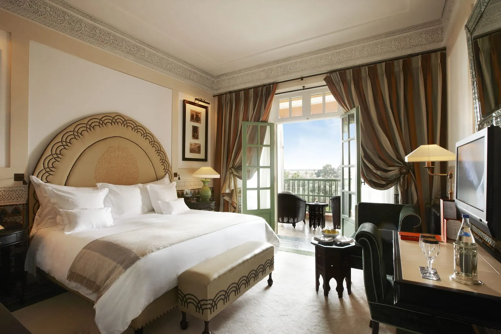 Agdal Deluxe Room at La Mamounia: a king bed under an arched carved headboard, with open doors to a balcony
