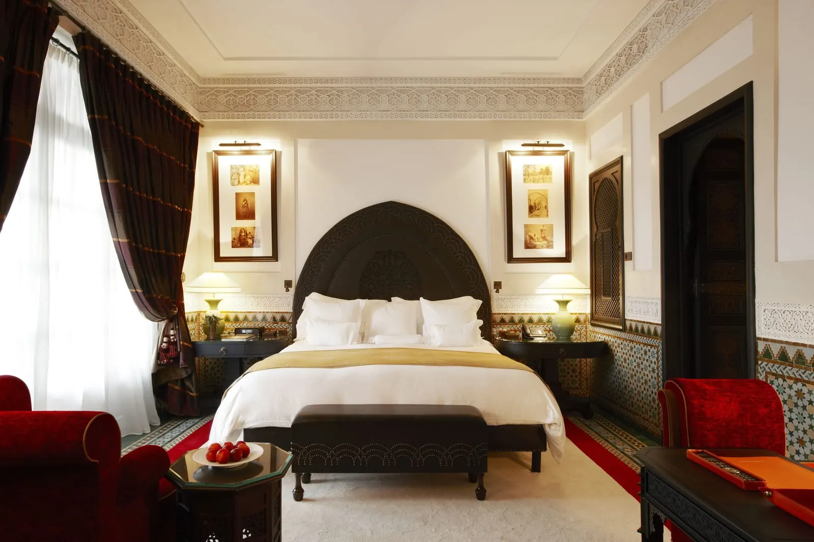 Executive Suite at La Mamounia: a king bed under a dark carved headboard, with red velvet armchairs and long curtains