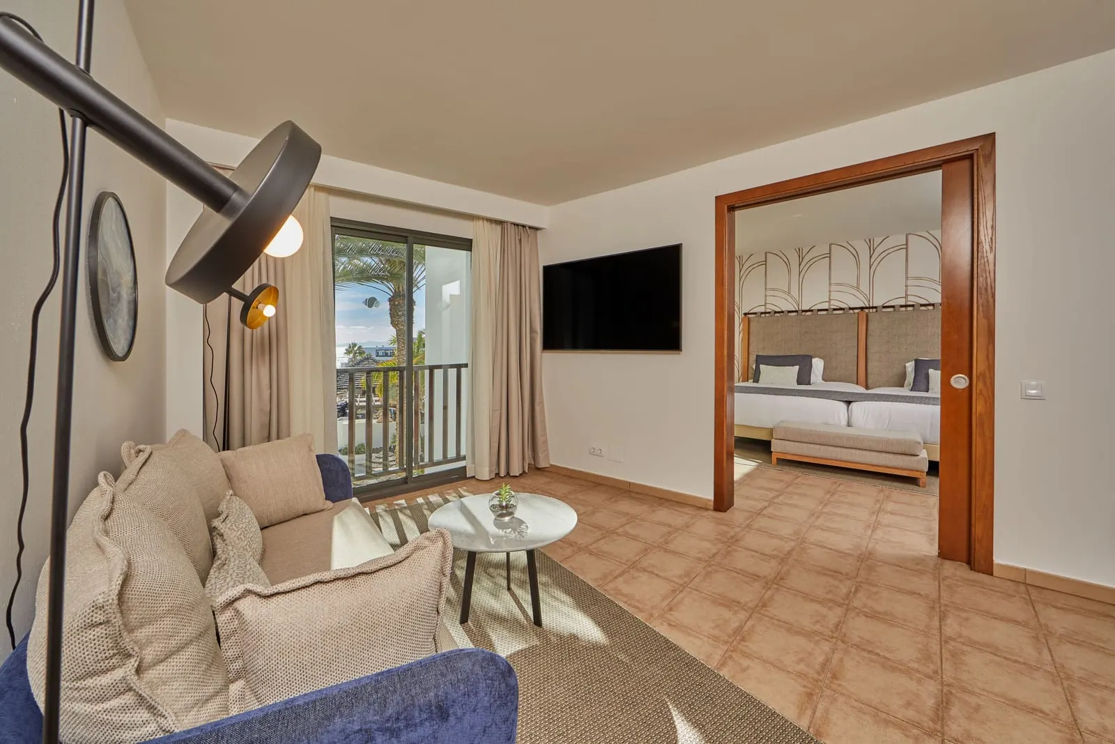 Preferred Club Suite Ocean View al Secrets Lanzarote Resort & Spa: un soggiorno separato con un divano, un tavolino e un televisore, con la camera visibile attraverso un'ampia porta