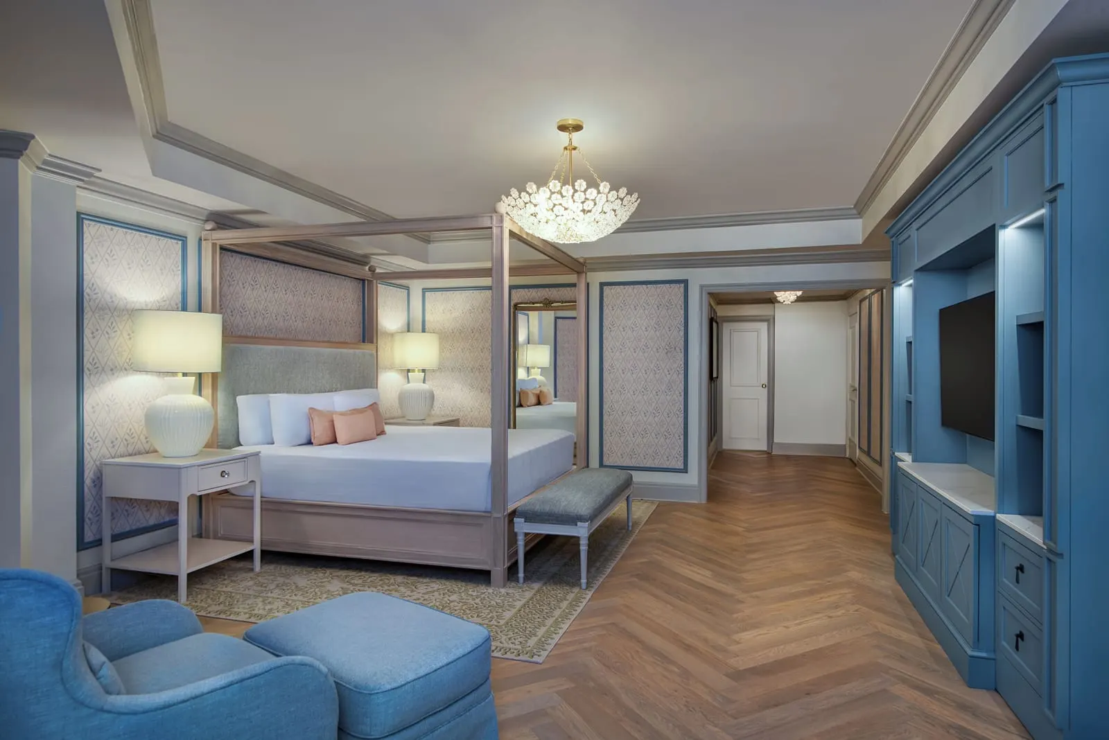 Disney Suite - Club Level at Disney's Grand Floridian Resort & Spa: a king bed in a pale wood four-poster frame, a blue armchair and footstool, and a built-in blue television cabinet along the hallway