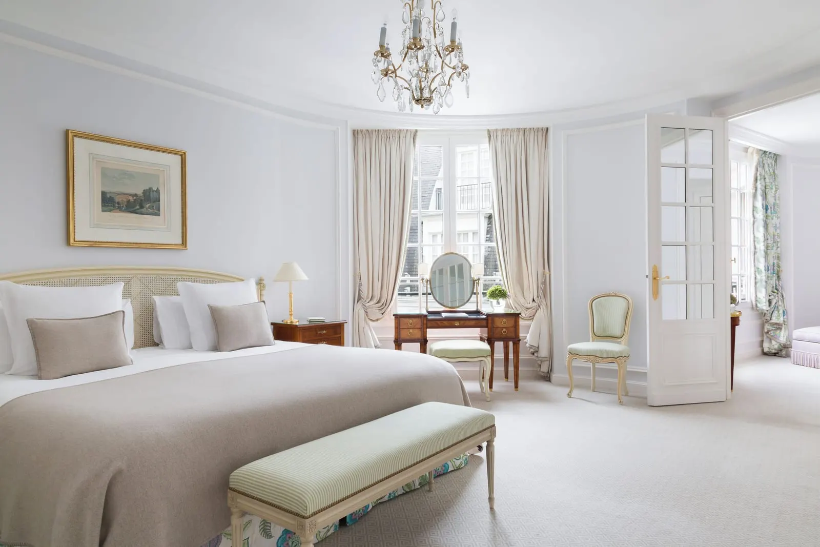 Suite Saint-Honoré at Le Bristol Paris: a bed with a taupe throw and a green bench, a dressing table between tall windows and a glazed door to the next room