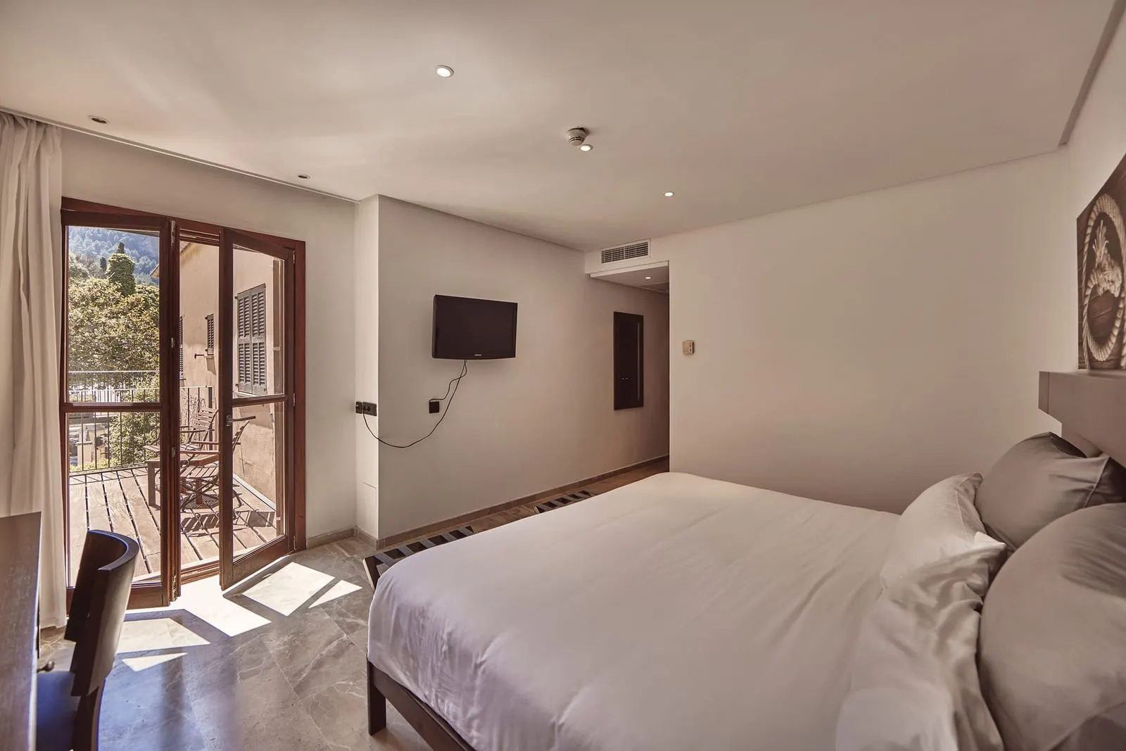 Traveler Nest at Maristel Hotel & Spa: a bed beside tall glazed doors that open onto a wooden balcony with chairs, a television on the wall