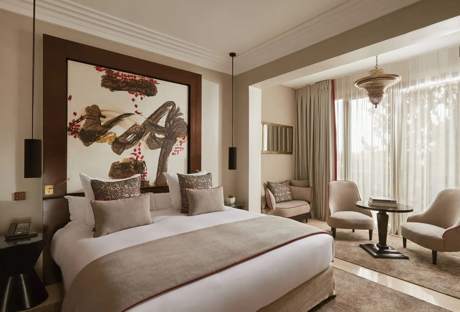 Junior Suite at Nobu Hotel Marrakech: a large bed under a calligraphy headboard panel, with two armchairs and a small table by sheer-curtained windows