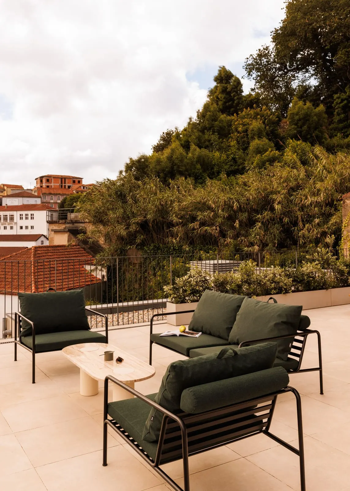 Two Bedroom Suite at The Rebello: a terrace with dark green outdoor armchairs, a low table and trees beyond